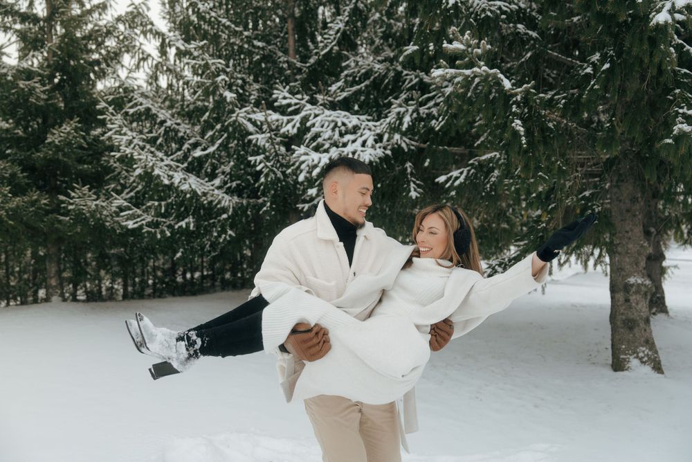 A couple enjoys a romantic winter photoshoot in a snow-covered forest landscape.