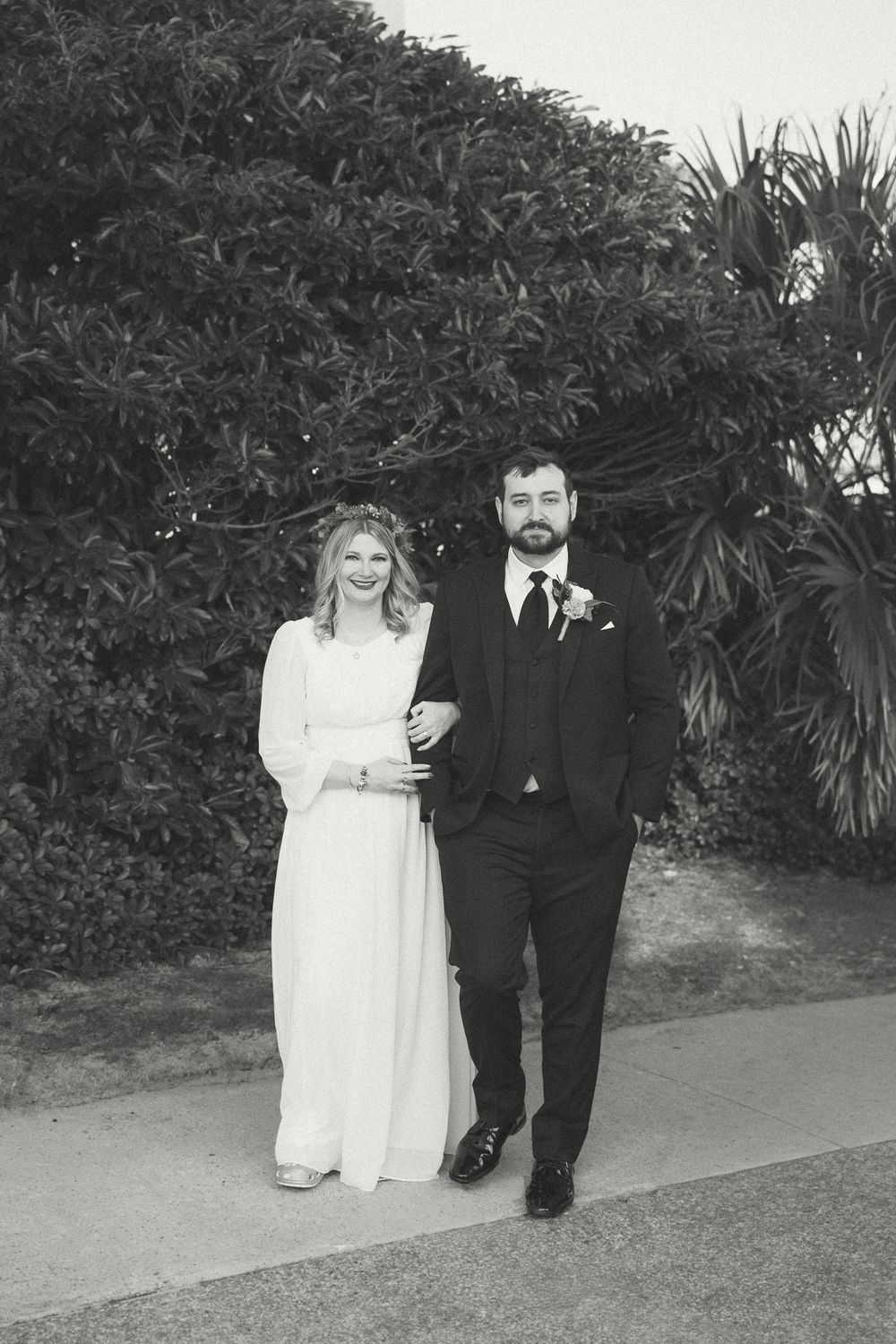 A couple in wedding attire walking together along a garden path in black and white photography. Wilmington, NC Wedding Photographer