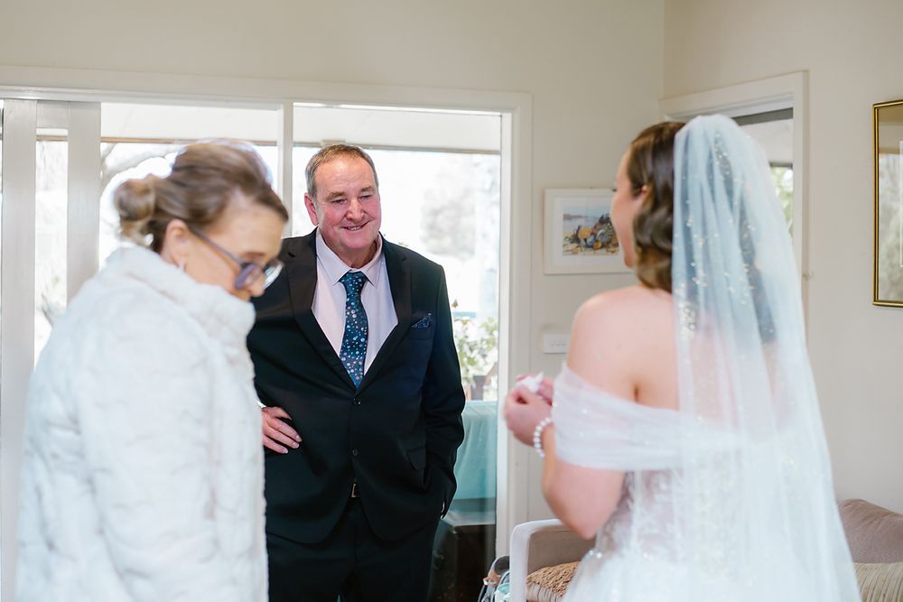 Wedding day first look scene in a bright room with large windows and white decor.