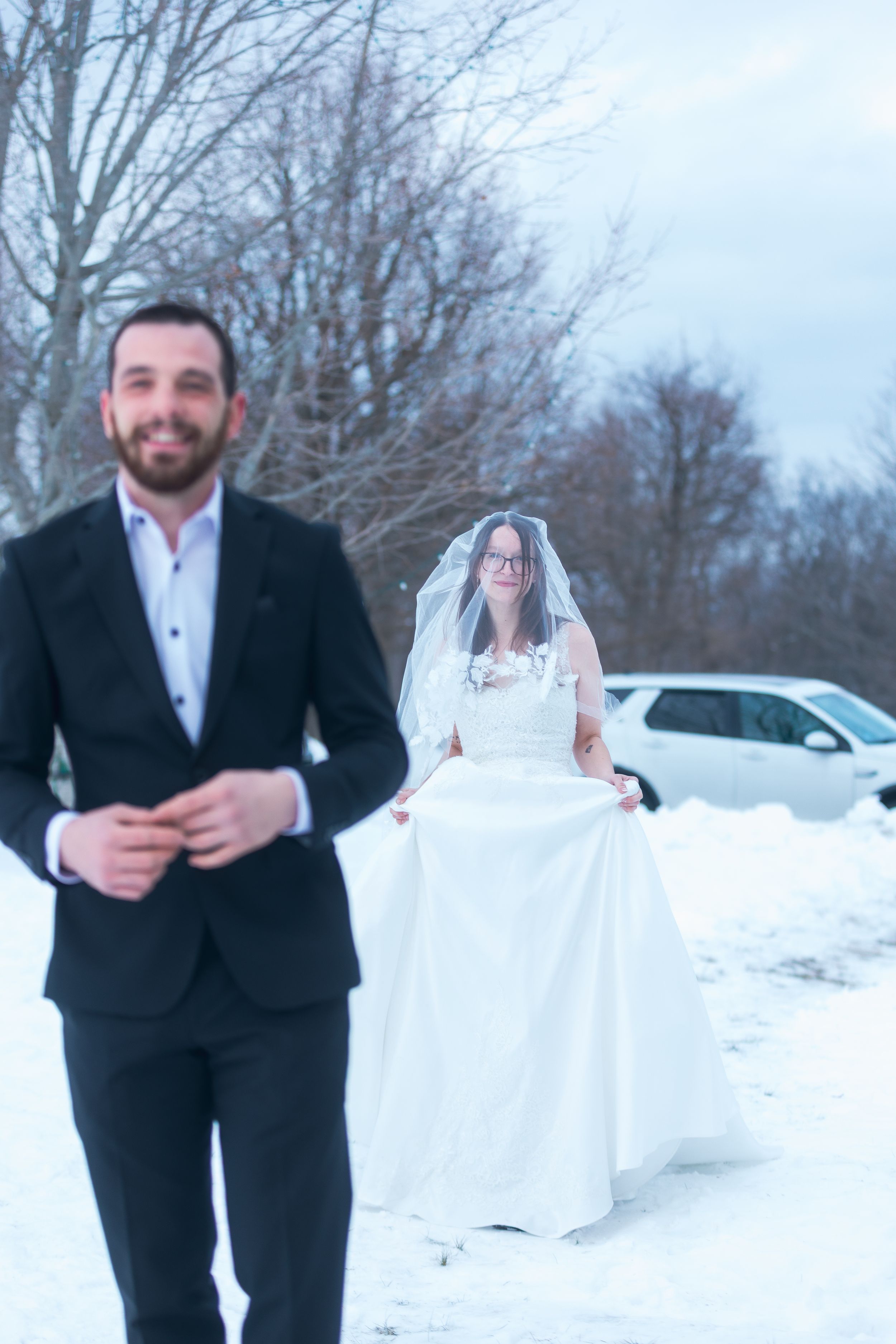 A couple poses playfully in formal attire against a snowy winter backdrop.