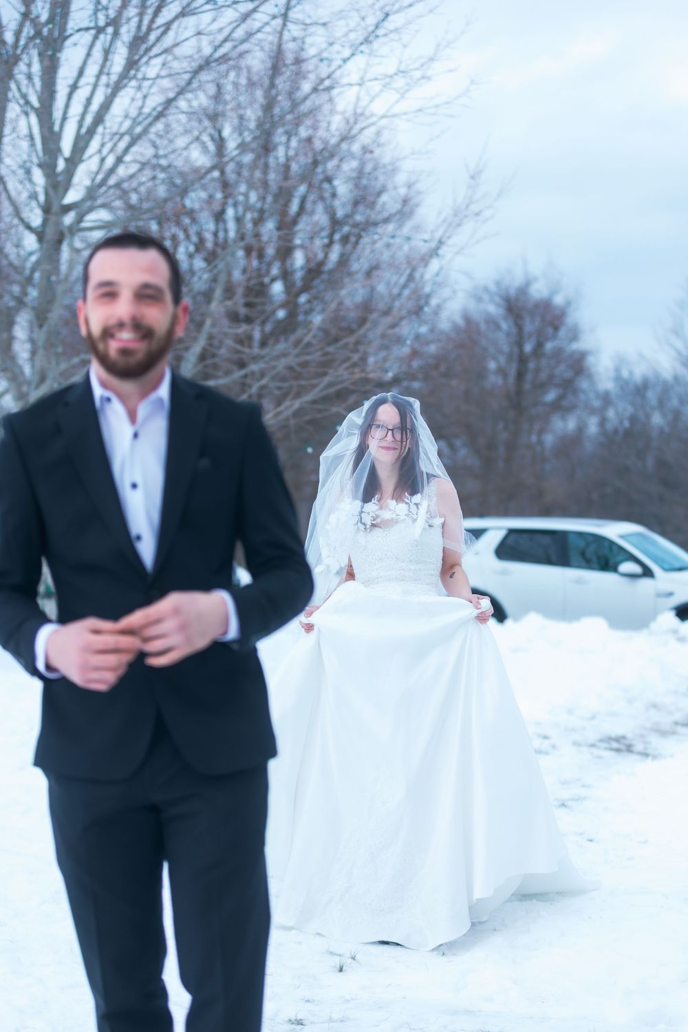 A couple poses playfully in formal attire against a snowy winter backdrop.