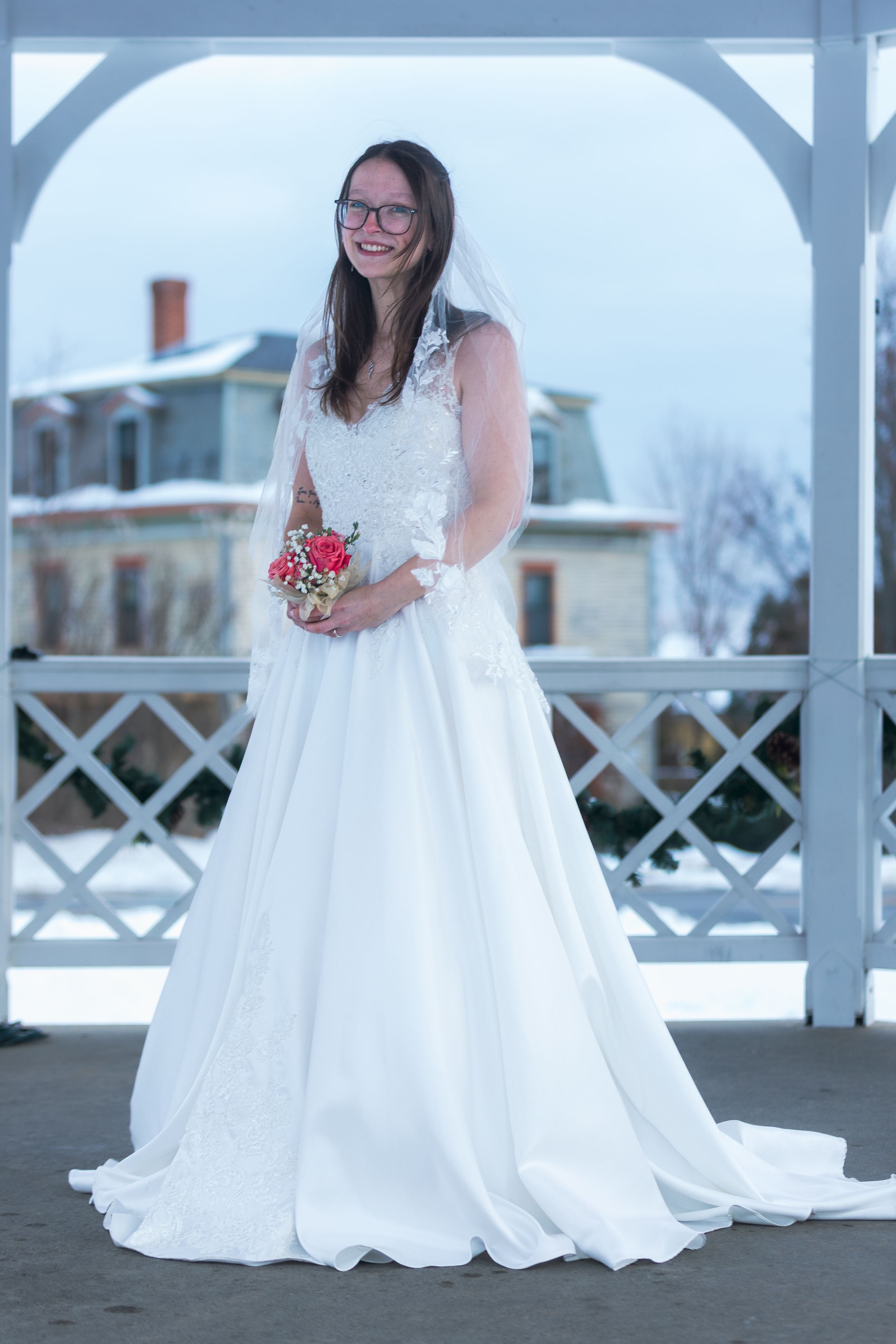 A winter wedding photo series showing a bride in a white lace gown posing in front of a snow-covered gazebo.