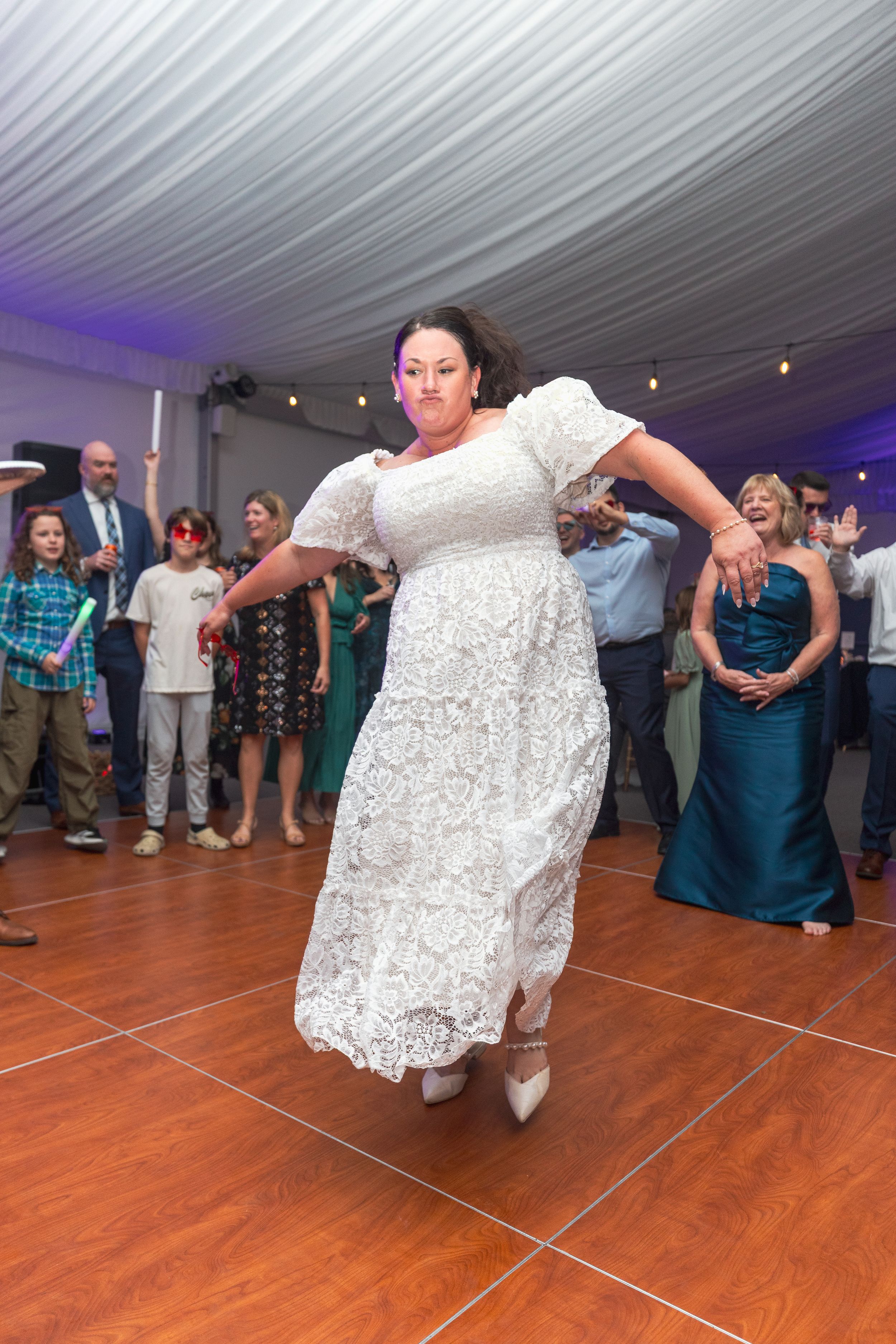 Wedding guests dance and celebrate on a wooden dance floor at a reception with blue lighting and white decor.