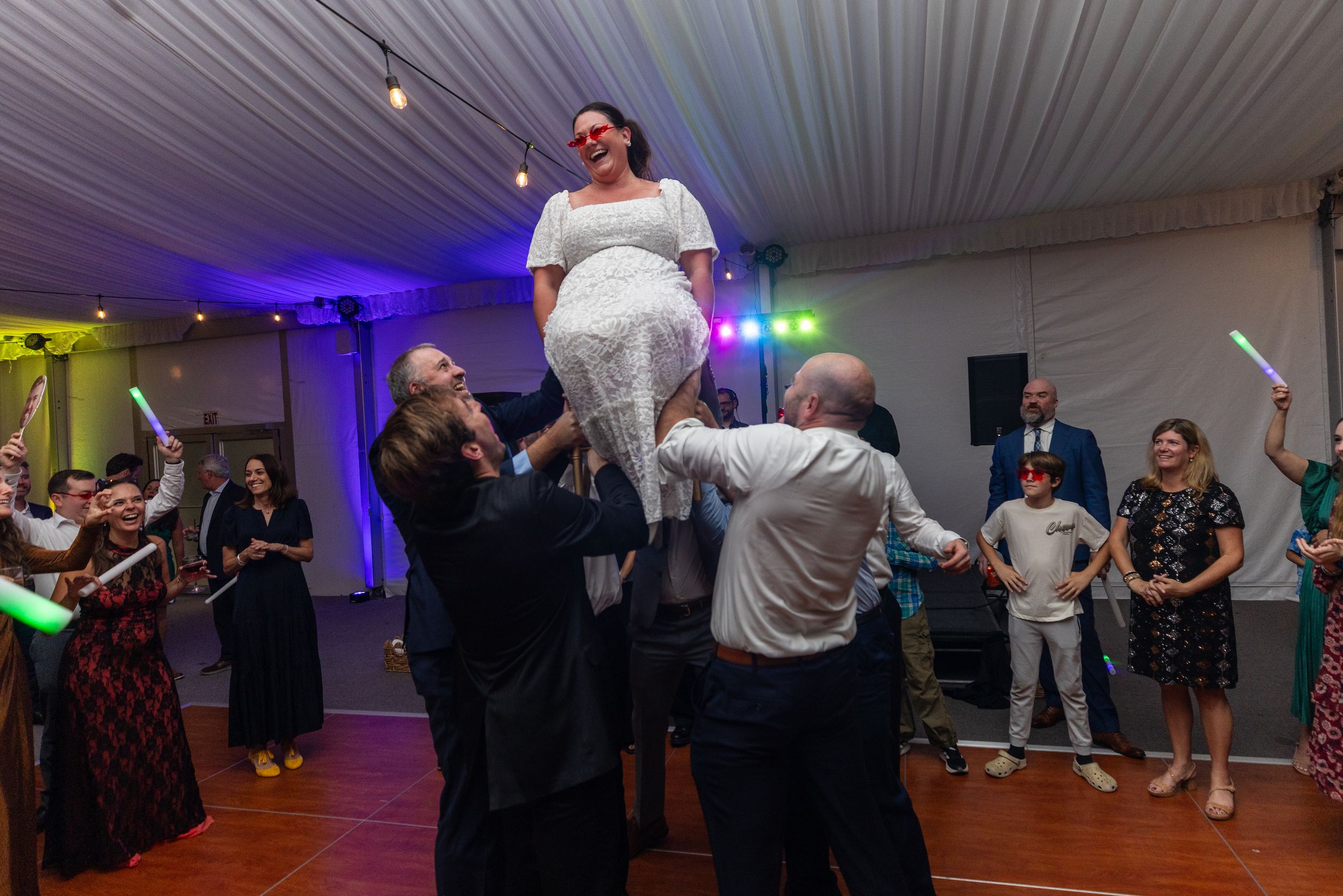 People dancing and socializing at an indoor party venue with colorful lighting and draped fabric ceiling decor.