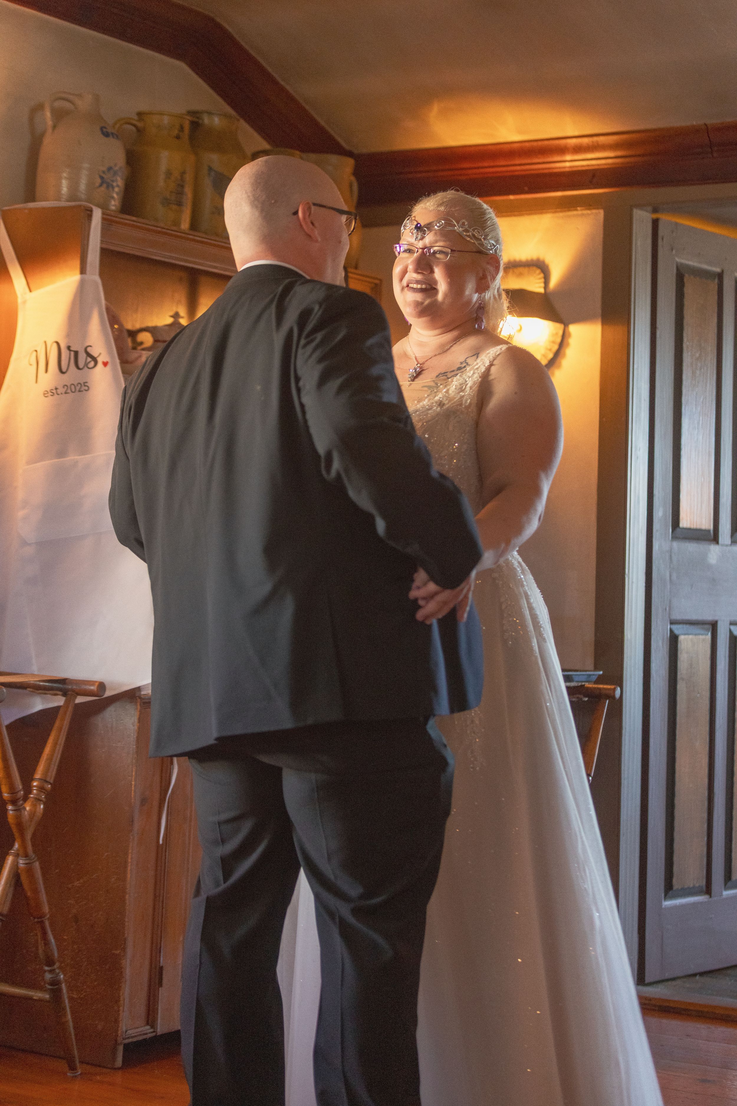 A couple shares an intimate moment during their first dance at a rustic indoor wedding venue with warm lighting.