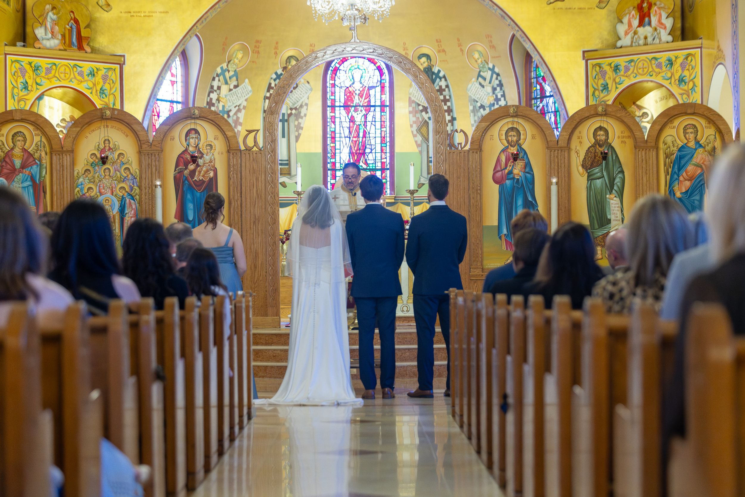 A wedding ceremony takes place in a beautiful Catholic church with golden walls and stained glass windows.