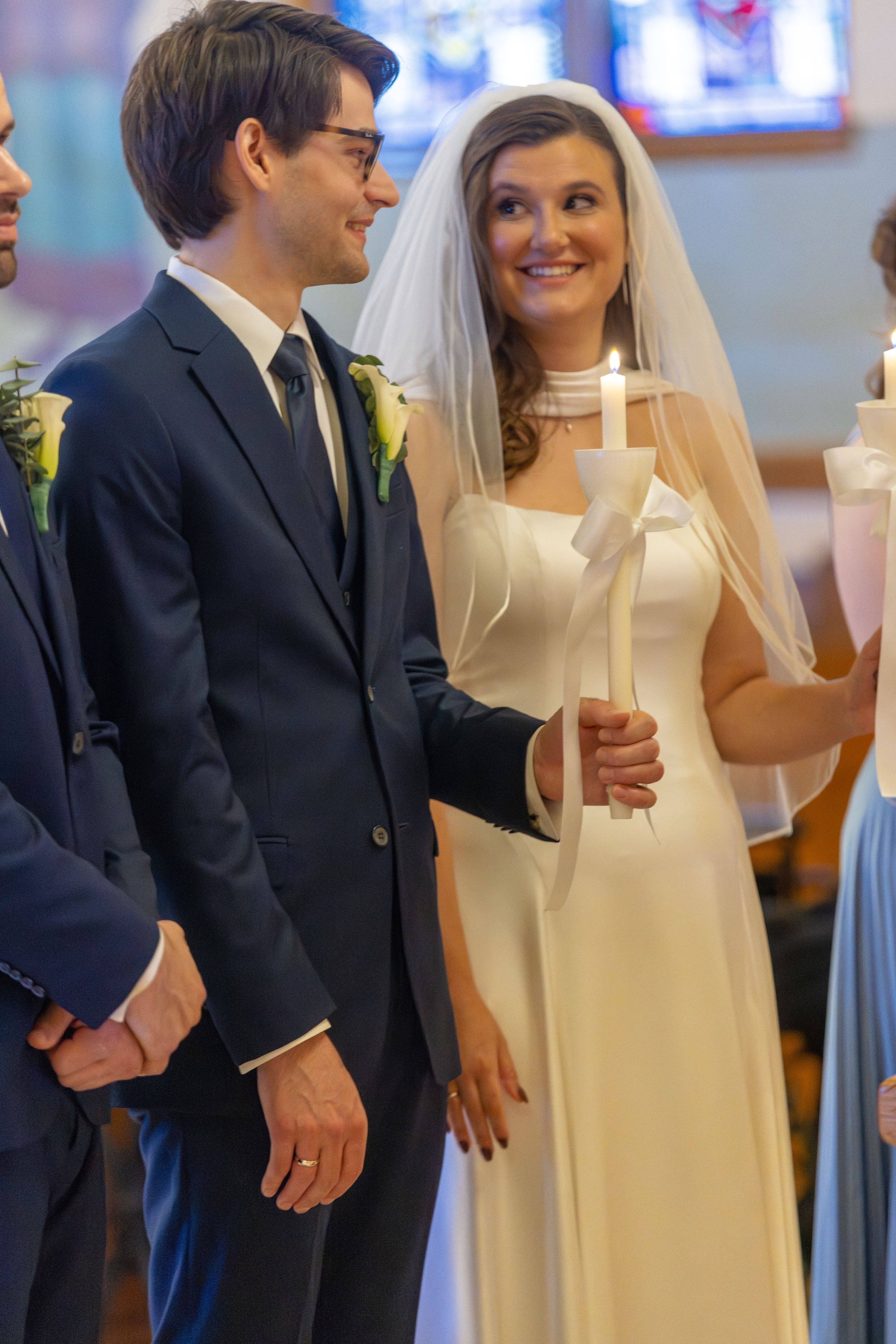 A bride in a simple white dress and groom in a navy suit share joyful moments during their wedding ceremony.
