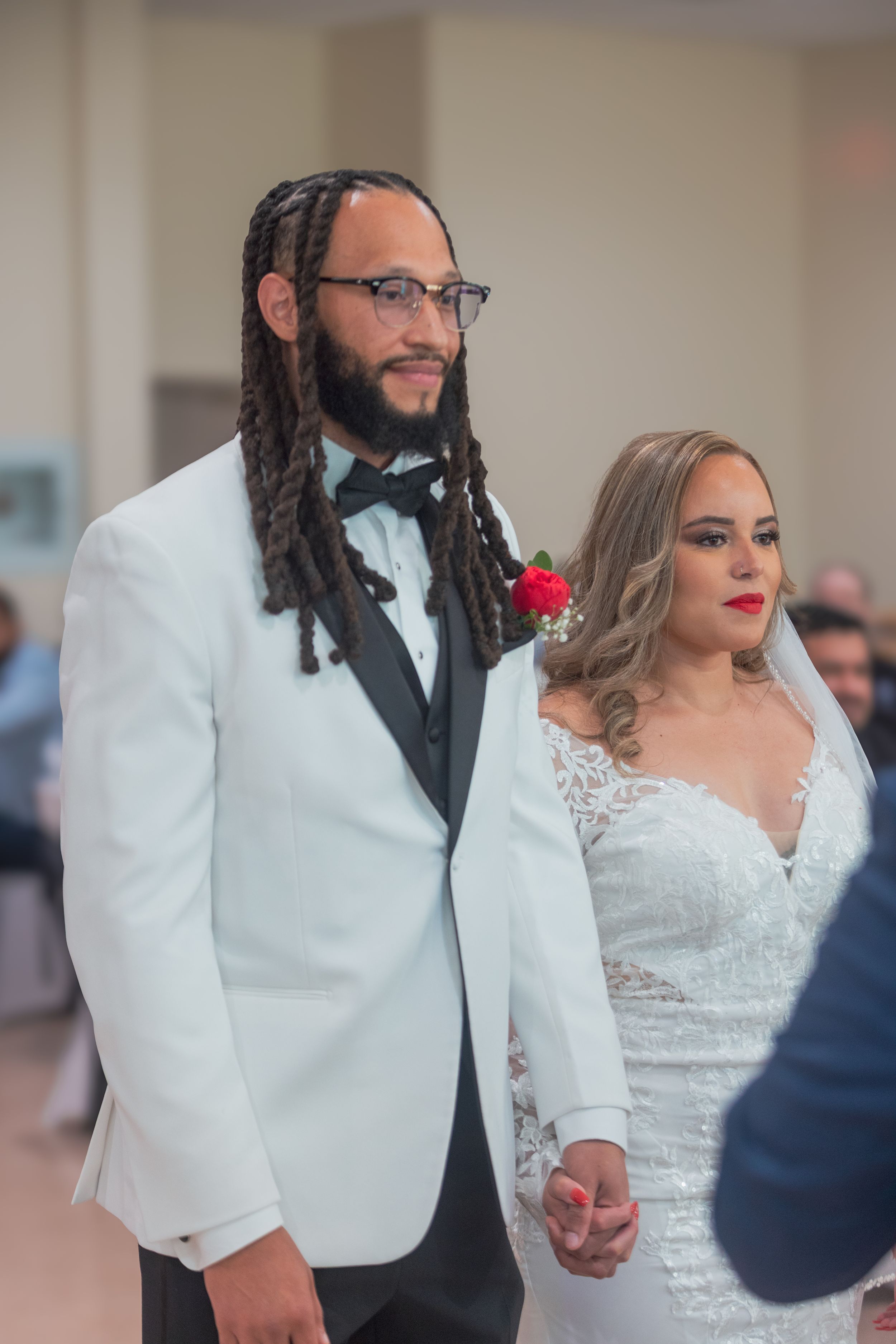 A wedding couple in elegant attire with the groom wearing a white tuxedo jacket and the bride in a lace wedding gown.