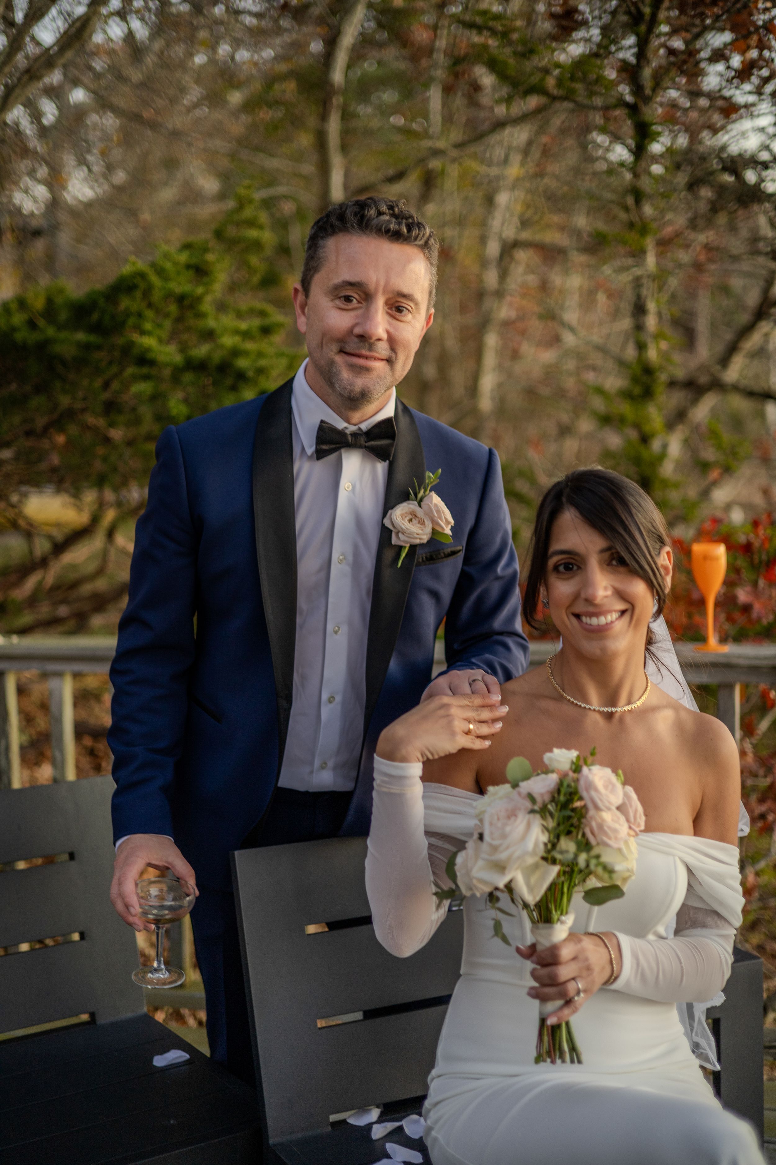 A couple in wedding attire share a celebratory moment with drinks on an outdoor patio.