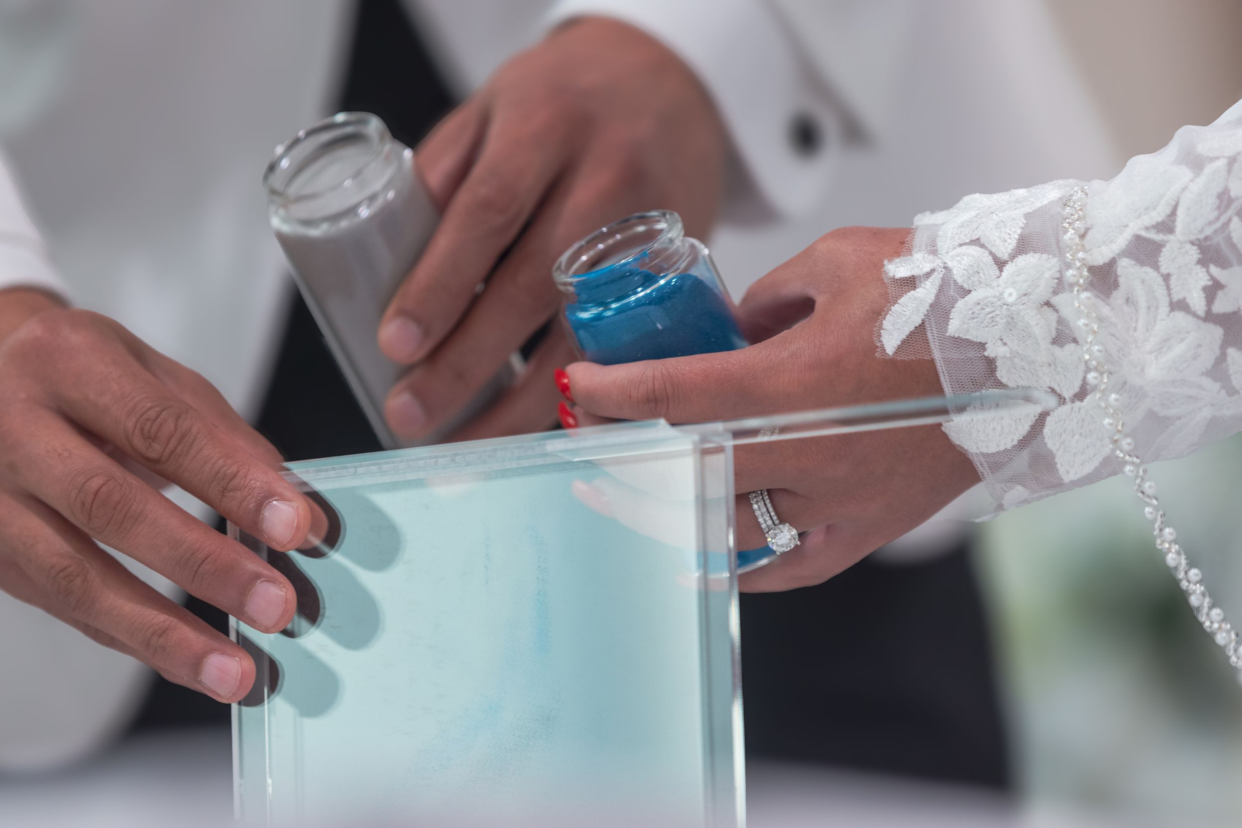Hands rolling up a blue colored dough on a white surface using a rolling pin.