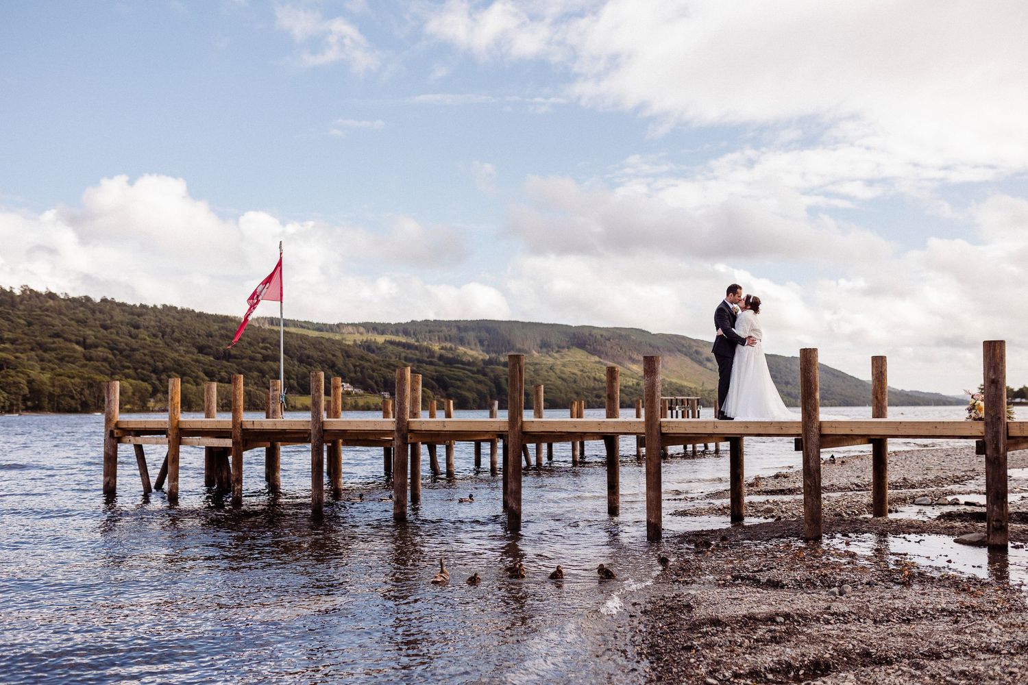 A series of wooden dock posts line up along a calm lake with mountains in the background under a blue sky.