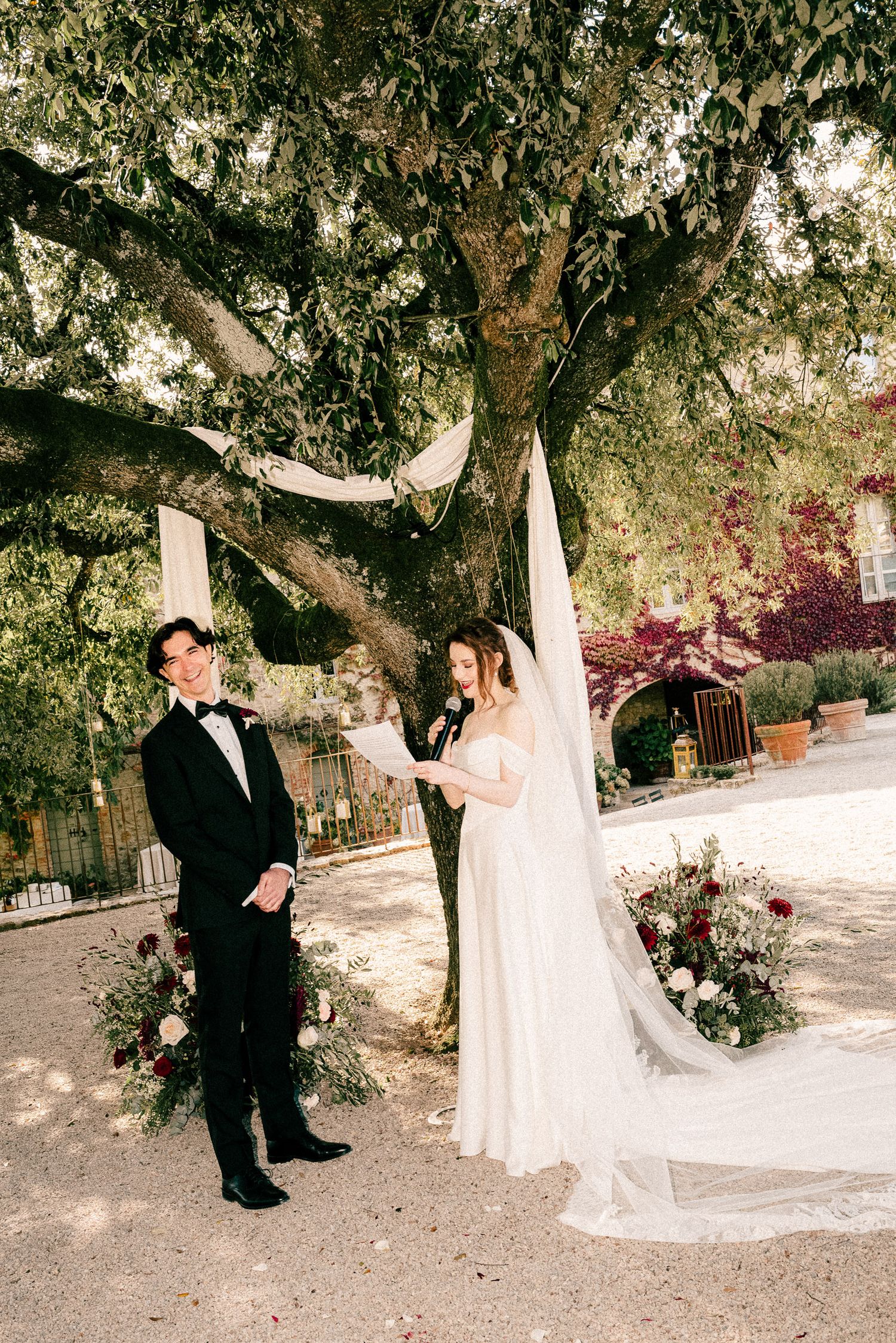A romantic wedding photo series showing a couple embracing under a majestic oak tree with flowing white drapery.