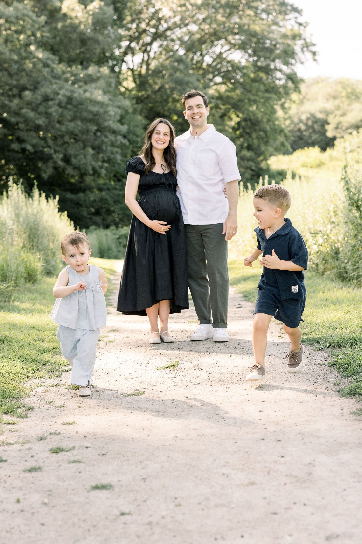A family enjoying a playful moment together on a dirt path surrounded by lush greenery on a sunny afternoon.
