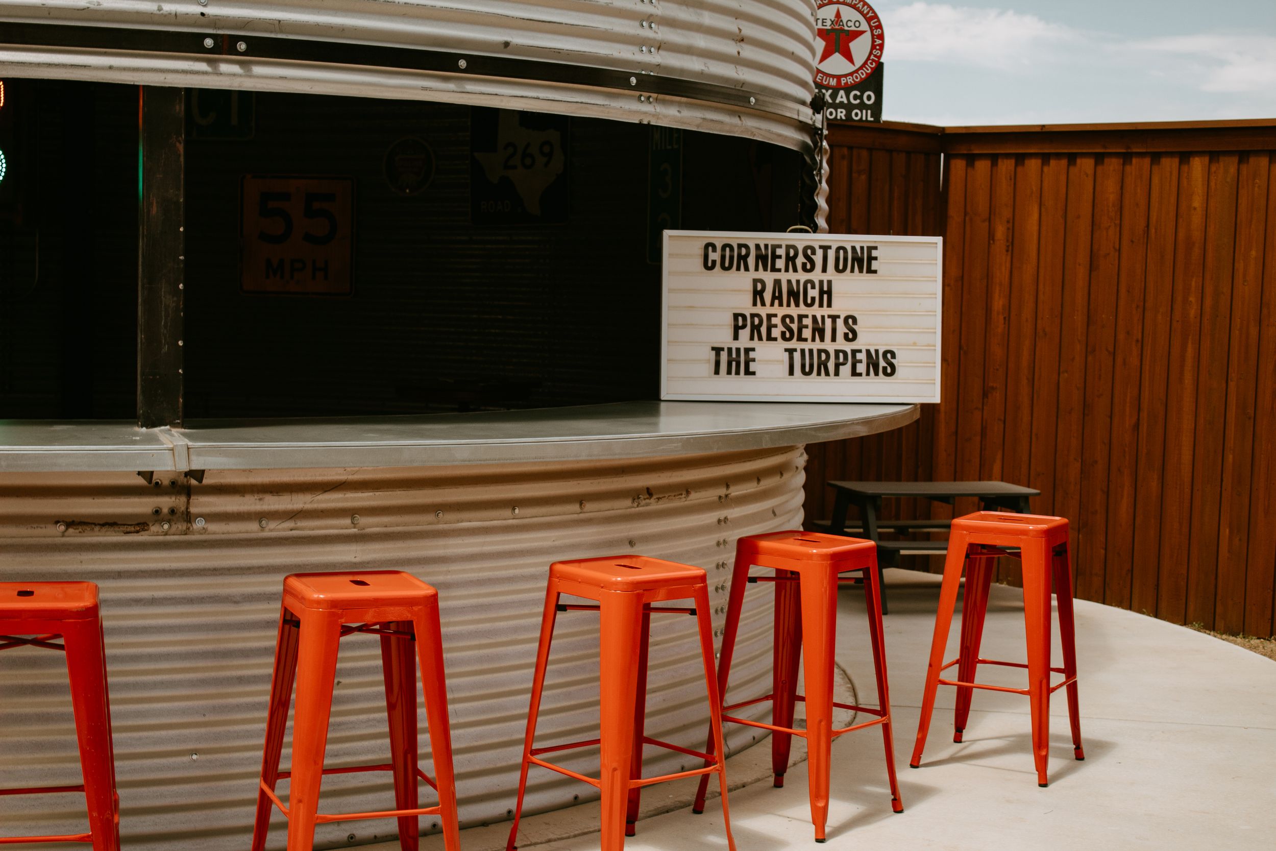 Orange bar stools outside Cornerstone Ranch venue with a marquee sign presenting The Turpens.