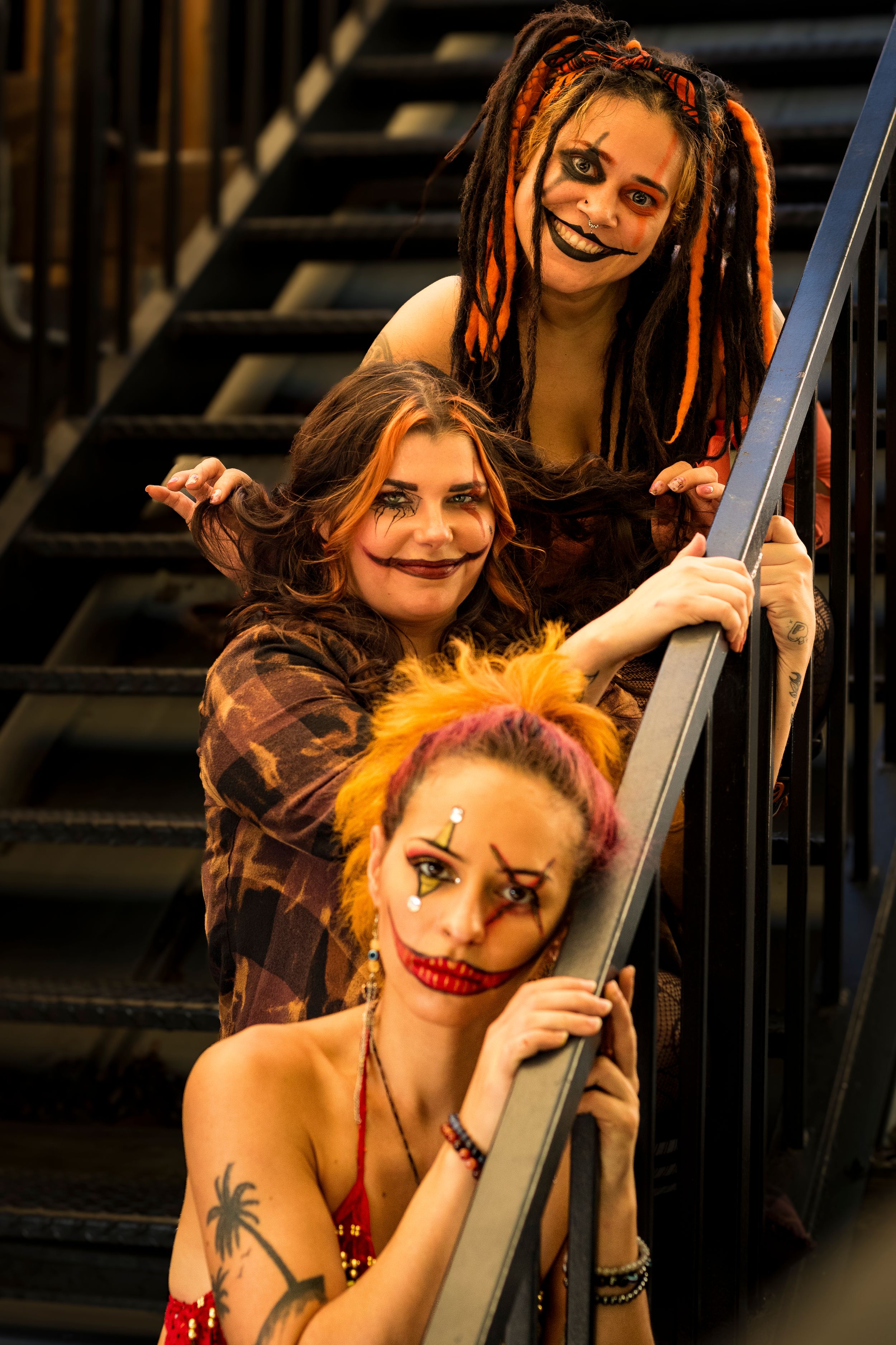 Three women in creepy clown Halloween makeup pose on dark staircase.