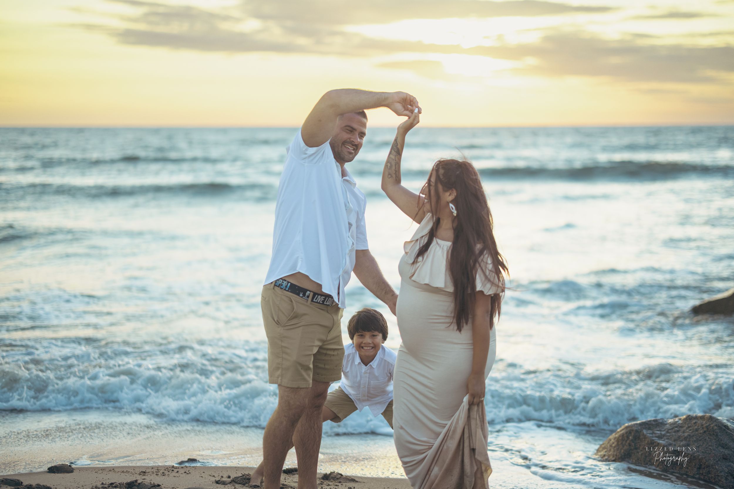 Couple dancing on beach at sunset while young son plays nearby.
