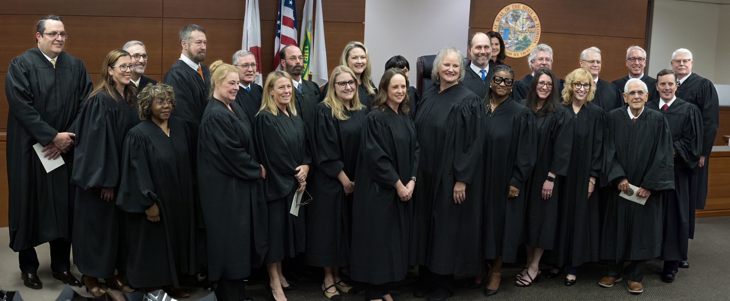 Large group of judges in black robes posing together for a formal group photo in a courtroom.