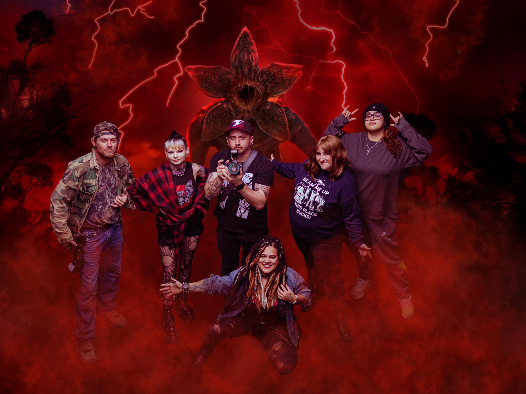 Group of six people posing dramatically in Halloween costumes with red lightning and monster backdrop.