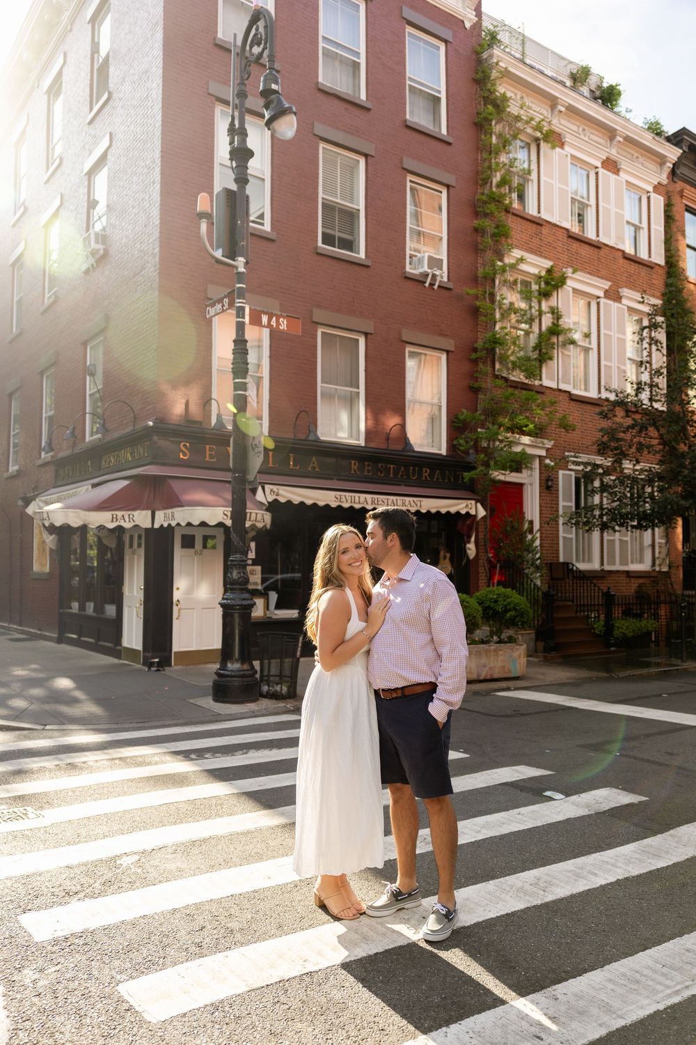 A couple shares a romantic moment on a crosswalk in a charming urban neighborhood with brick buildings.