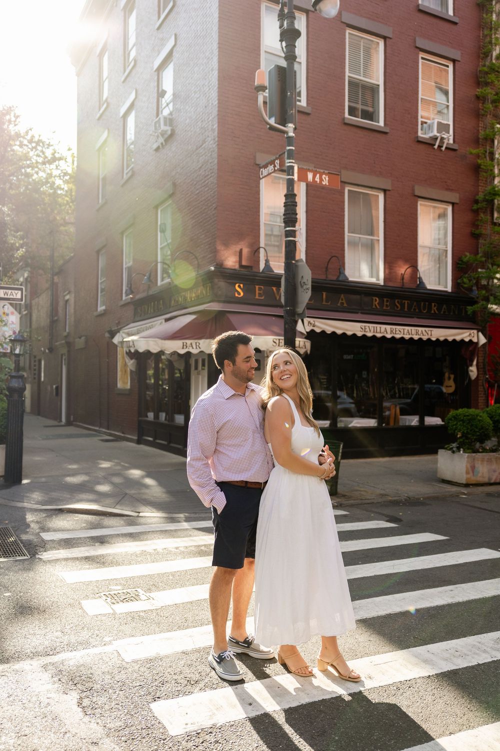 A couple stands on a crosswalk in front of a New York City corner restaurant on a sunny afternoon.