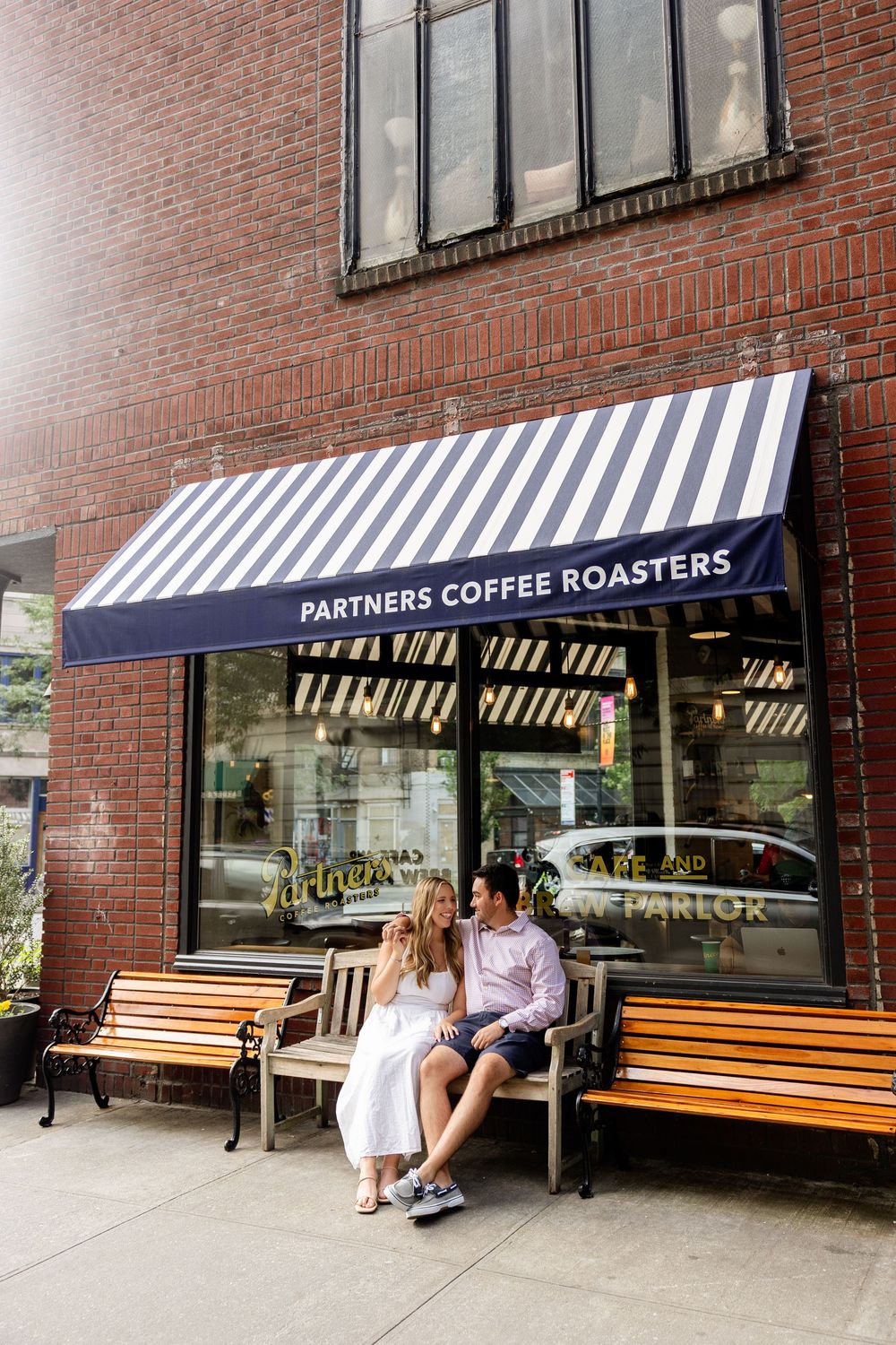 A striped awning over wooden benches outside Partners Coffee Roasters storefront on a brick building.