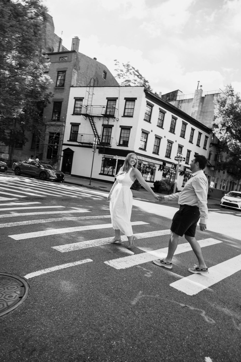 A sequence of black and white photos showing two people playfully crossing a pedestrian crosswalk in an urban setting.