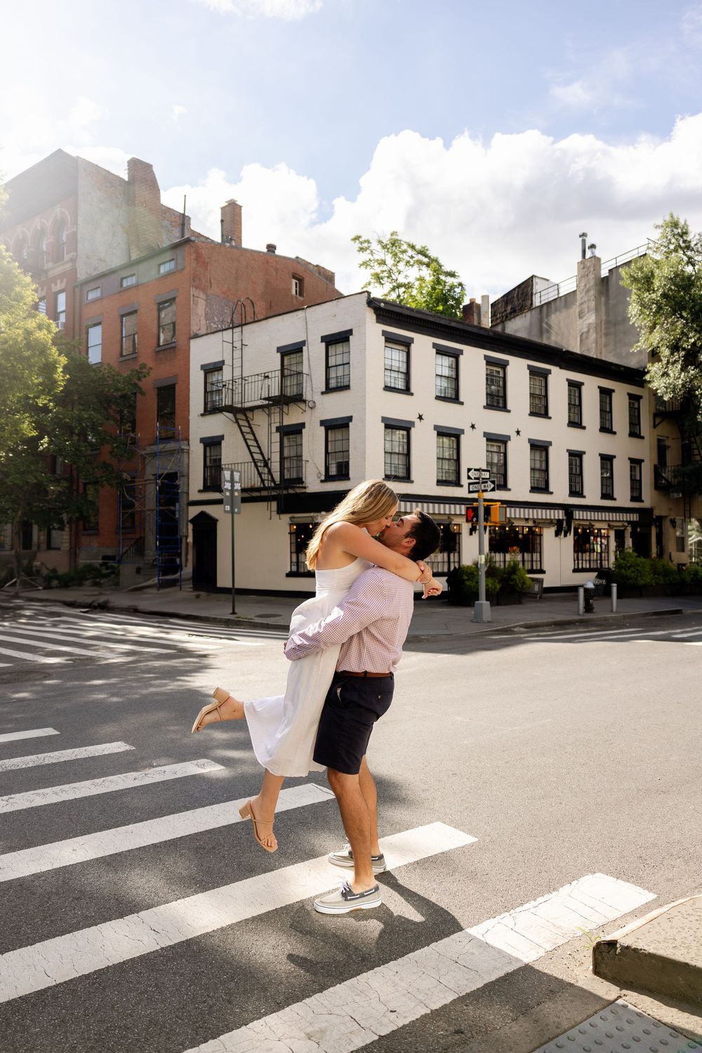 A couple dances playfully on a city street corner with historic brick buildings in the background.