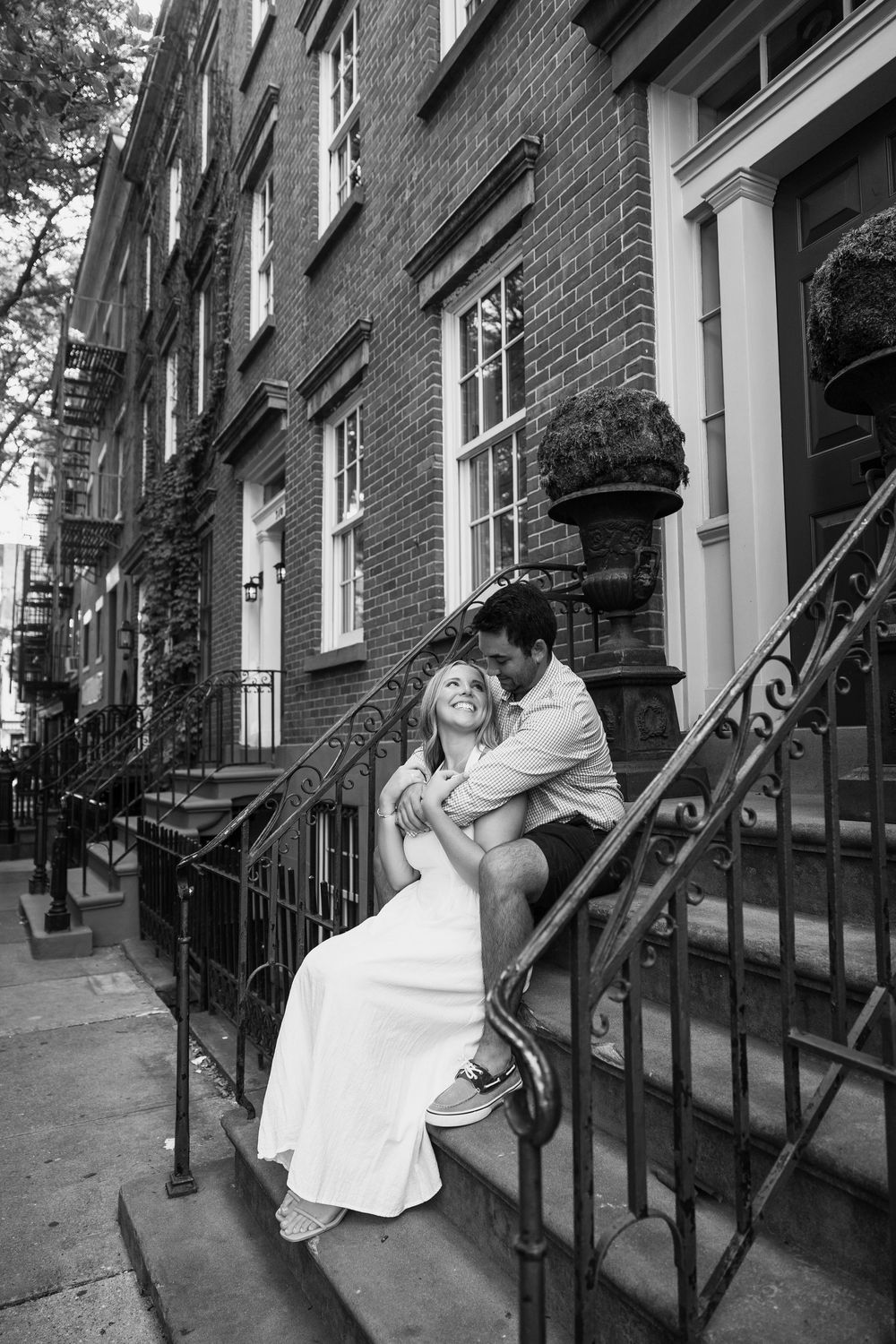 A couple shares a romantic moment on historic brownstone steps in black and white photography.