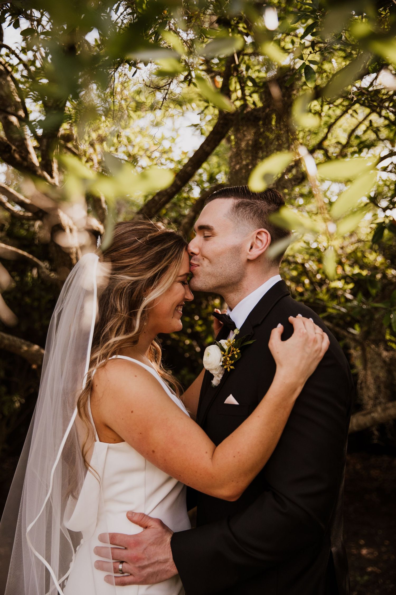 A bride and groom share a romantic kiss under a flowering tree on their wedding day.