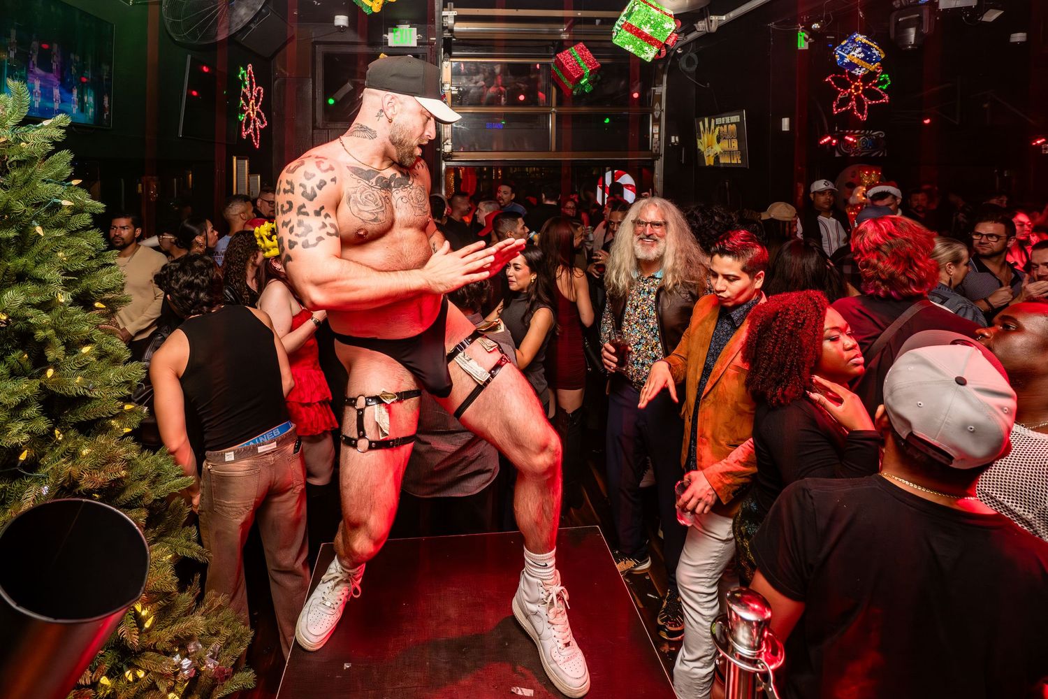 Shirtless gogo dancer stands on a platform box and dances for a crowd at FLICKS in San Diego