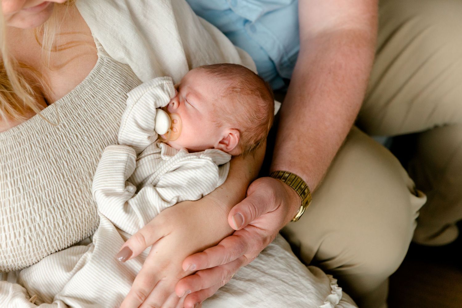 Newborn baby sleeping peacefully in parents arms during intimate lifestyle photography session.