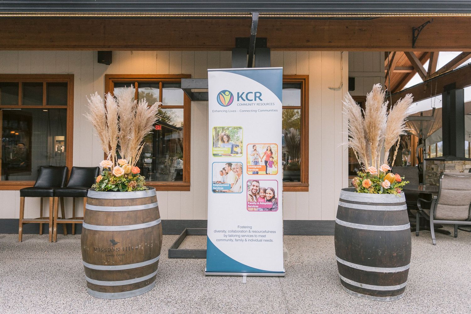 Row of rustic wooden wine barrels displayed along a covered outdoor walkway with decorative planters.
