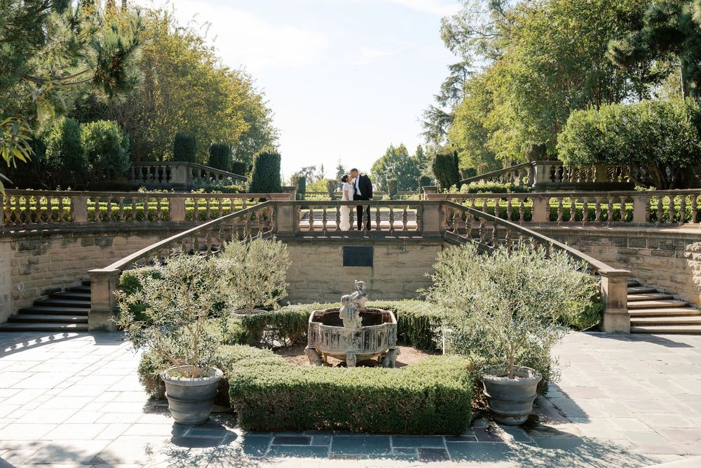 A panoramic view of a stone terrace garden with ornate railings and flowering plants in a formal garden setting.