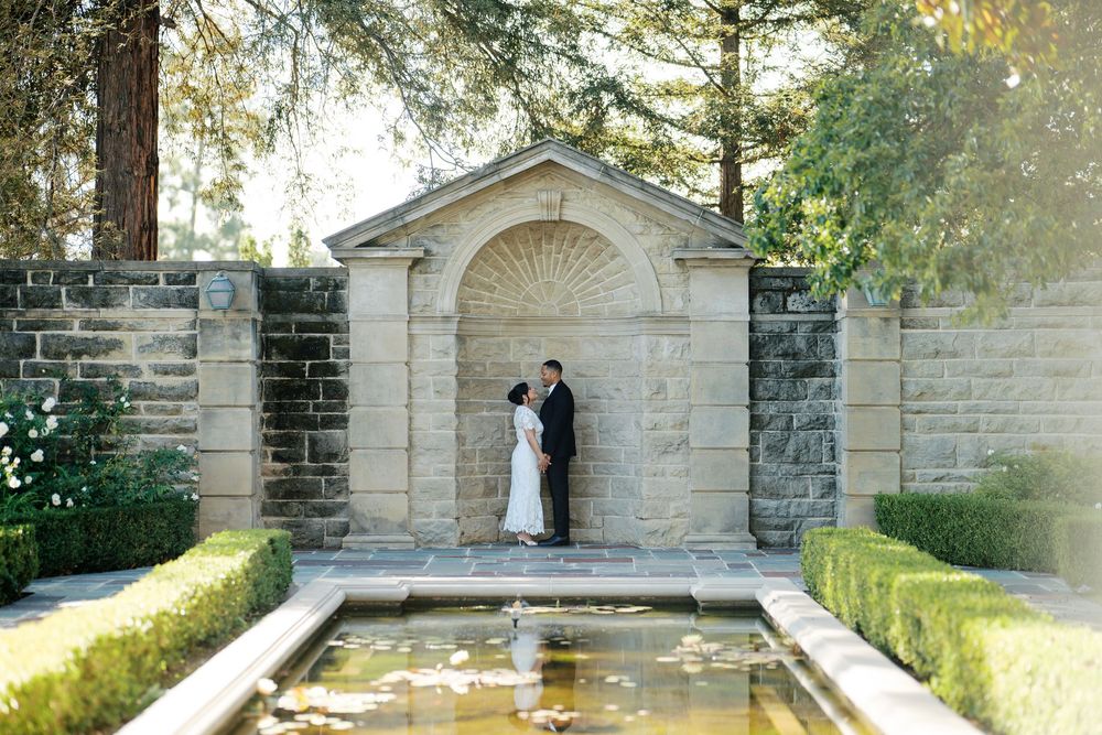 Stone archways and architectural features line a garden path in dappled sunlight.
