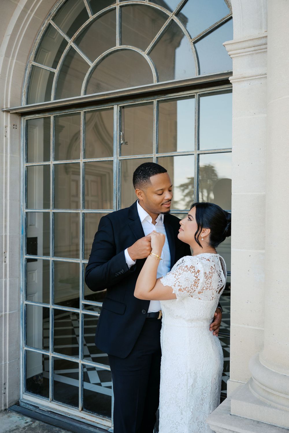A romantic moment captured in an elegant arched colonnade with large windows.