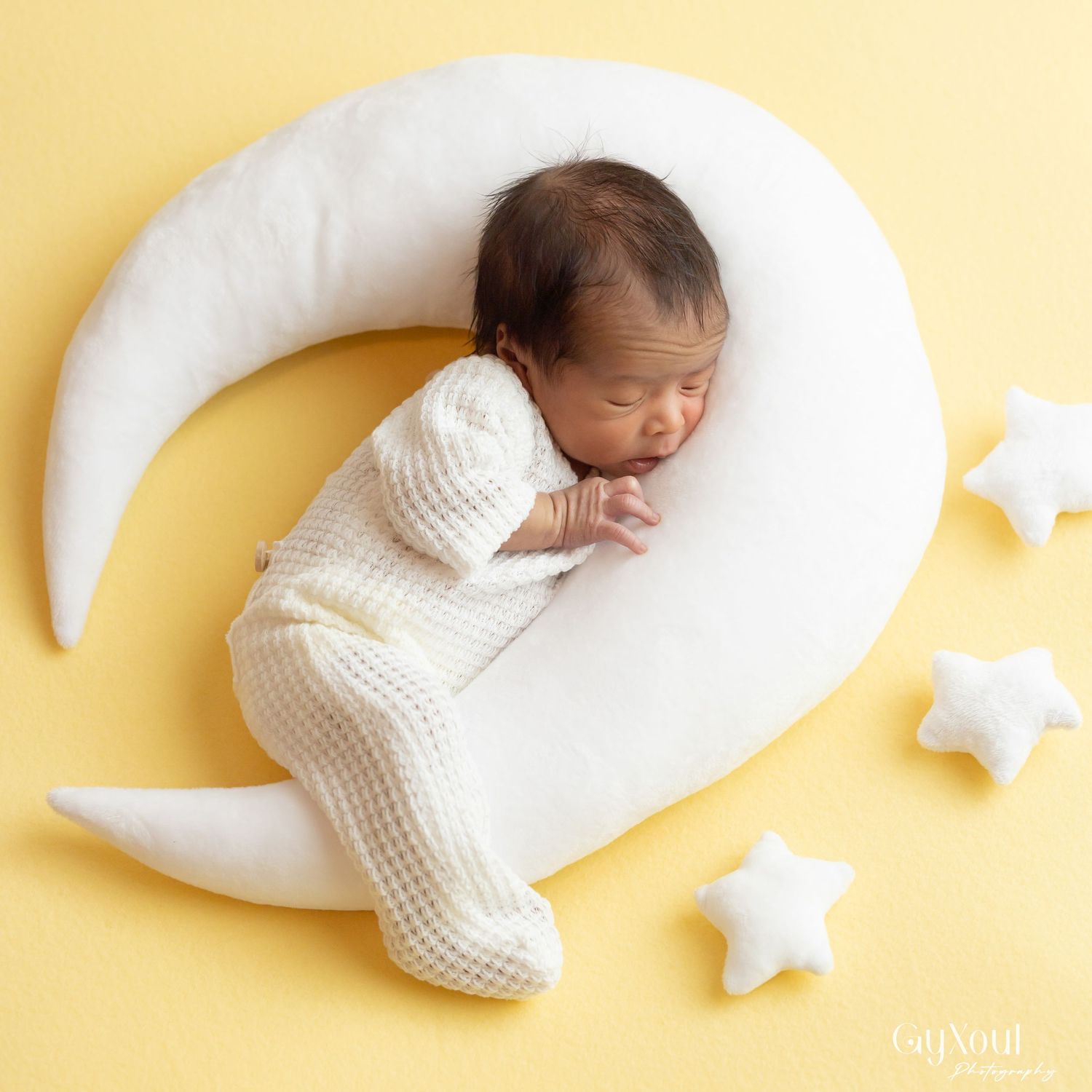 Baby sleeping peacefully on a white crescent-shaped nursing pillow with decorative star cushions on yellow background.