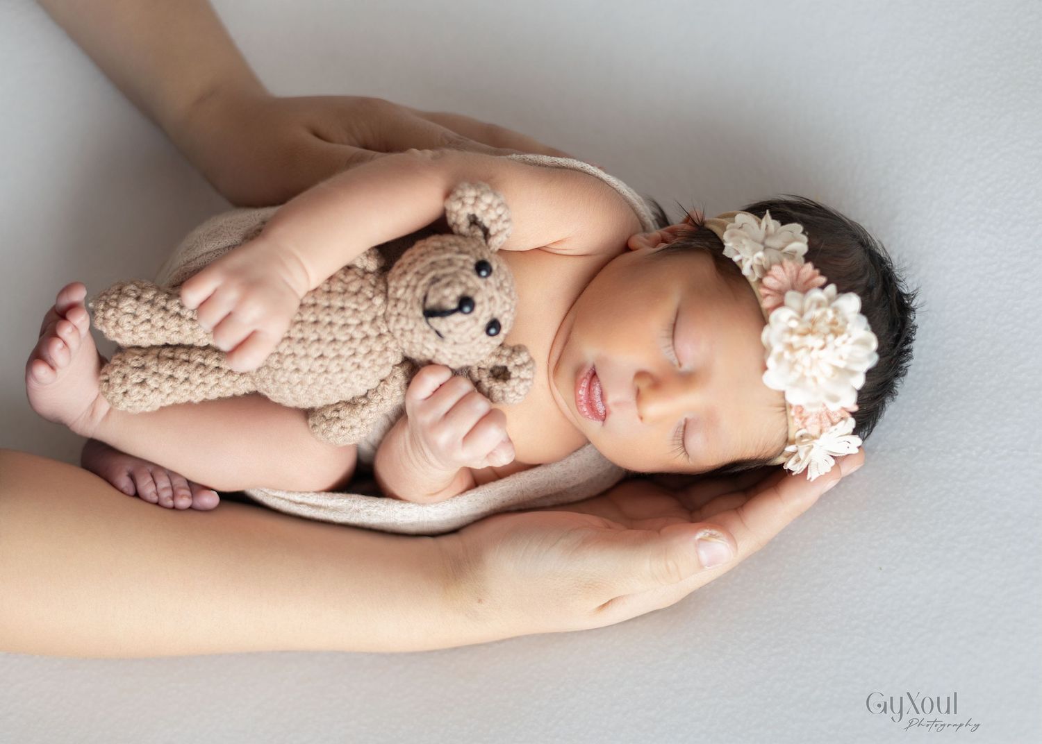Sleeping newborn baby lying on side wearing lace wrap and floral headband in soft pastel studio portraits.