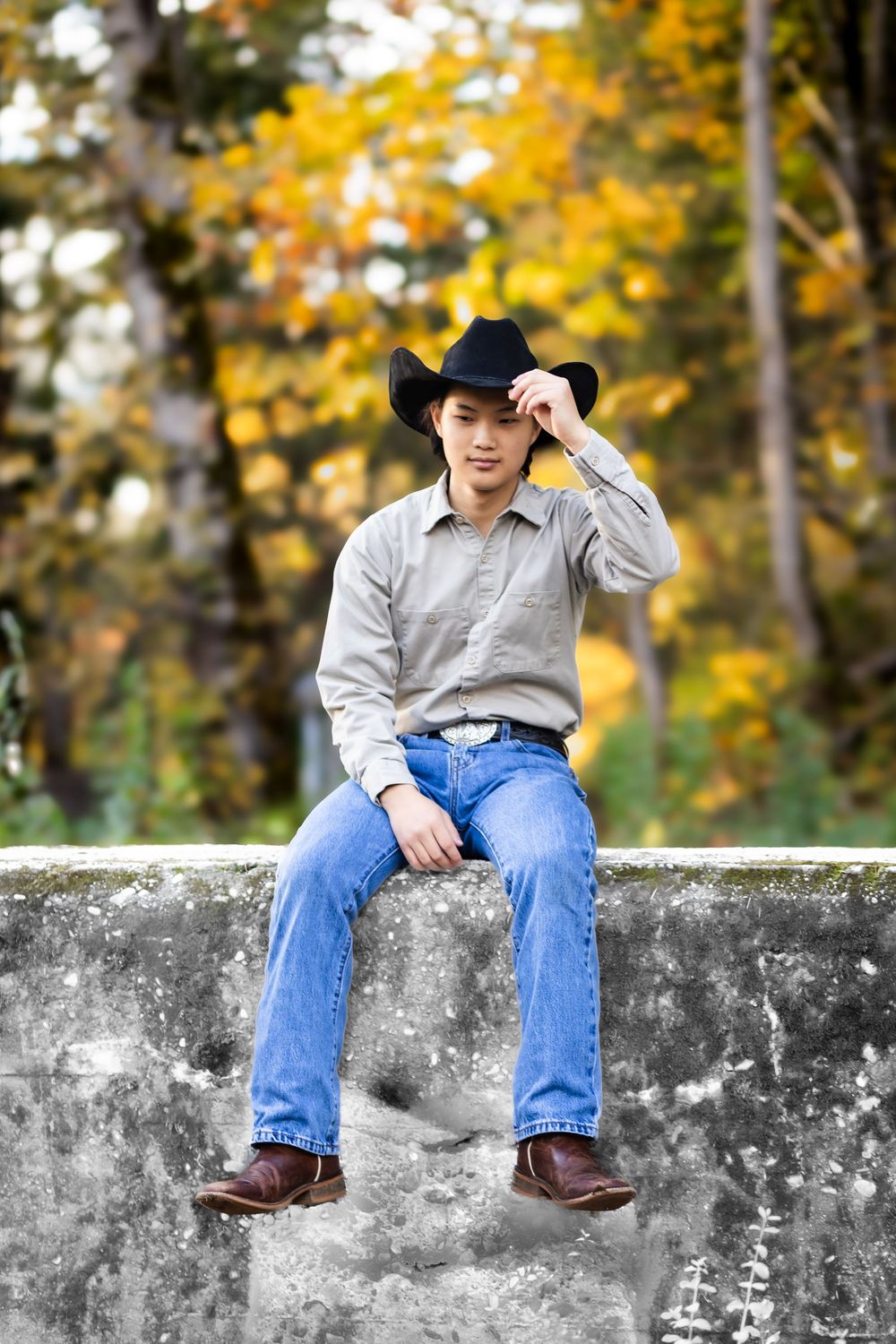 A person wearing a baseball cap and jeans sits on a stone wall with vibrant yellow autumn foliage in the background.