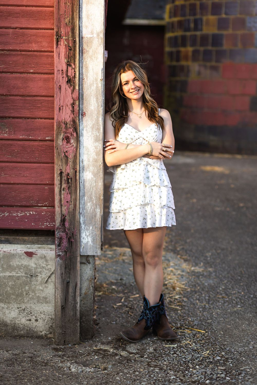 A rustic photo series against a red barn wall featuring someone in a floral dress and dark boots.