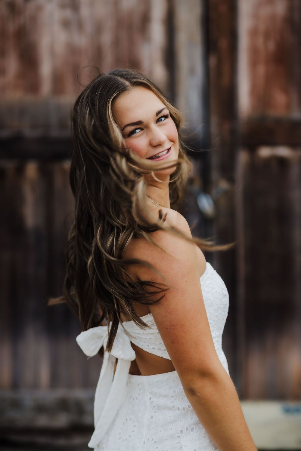 A joyful portrait of someone wearing a white eyelet dress with cutout details and a bow in the back.