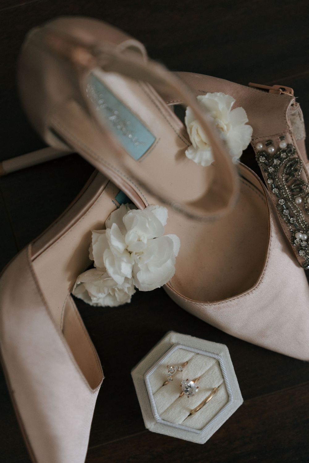 Elegant blush pink wedding shoes with white floral details displayed next to a hexagonal ring dish with engagement rings.