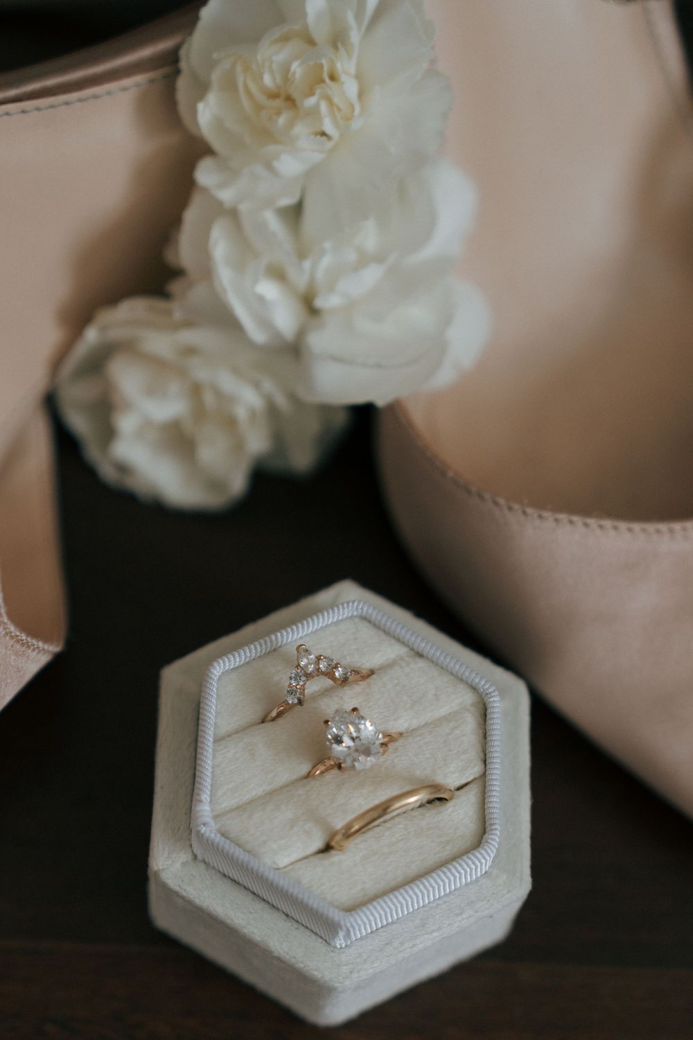 Wedding ring displayed in hexagonal velvet ring box with white floral decor and blush pink accents.