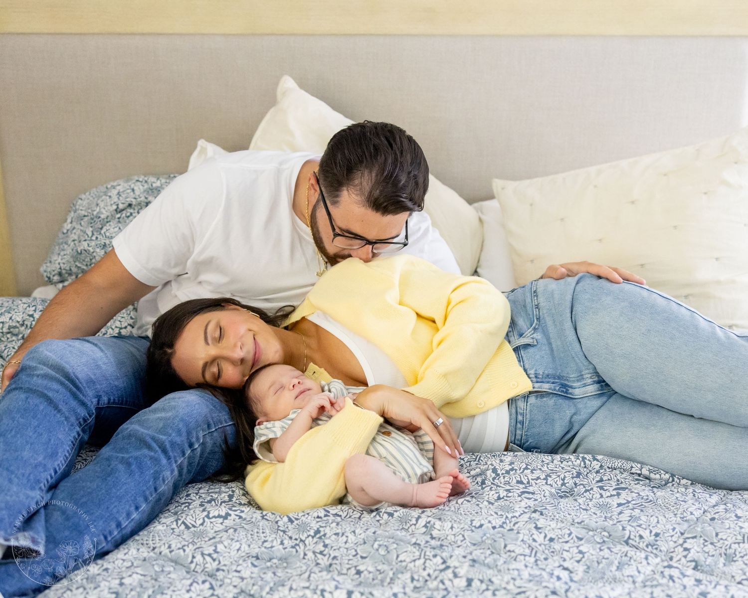 A couple stands by a window while lovingly holding their newborn baby in a tender family moment.