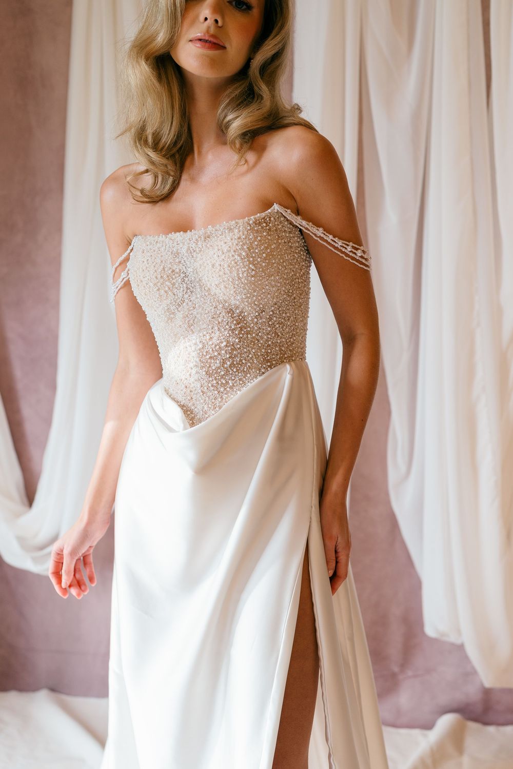Elegant white wedding dress with beaded bodice and flowing skirt displayed against drapes.
