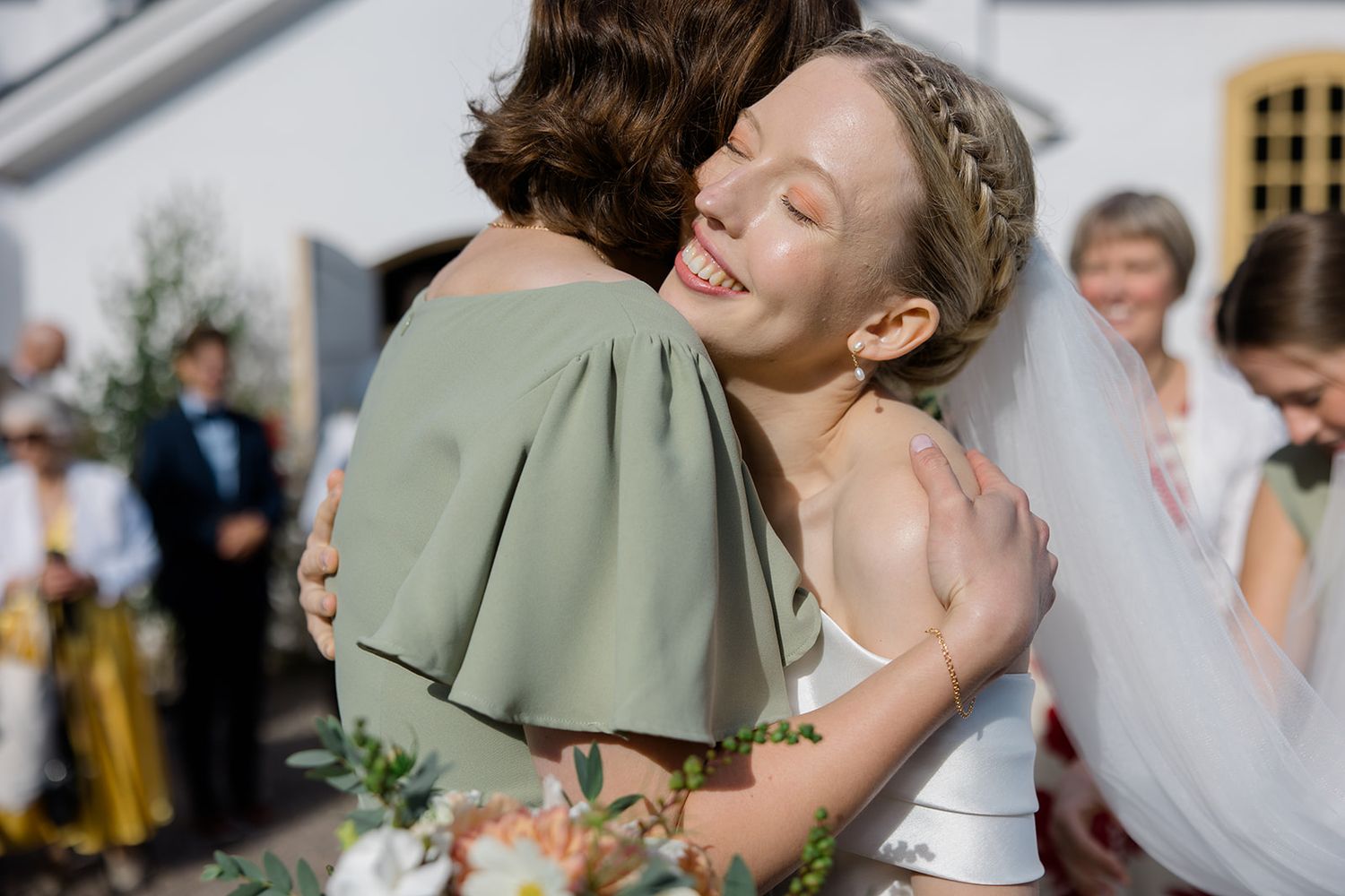 Two wedding guests share an emotional embrace at an outdoor reception celebration while other attendees look on.