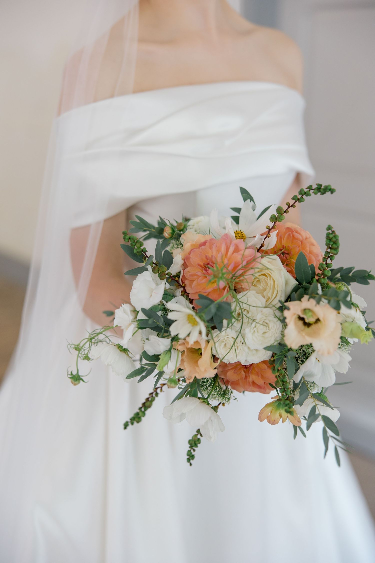 A romantic bridal bouquet with peach and cream flowers featuring garden roses, ranunculus and delicate greenery.