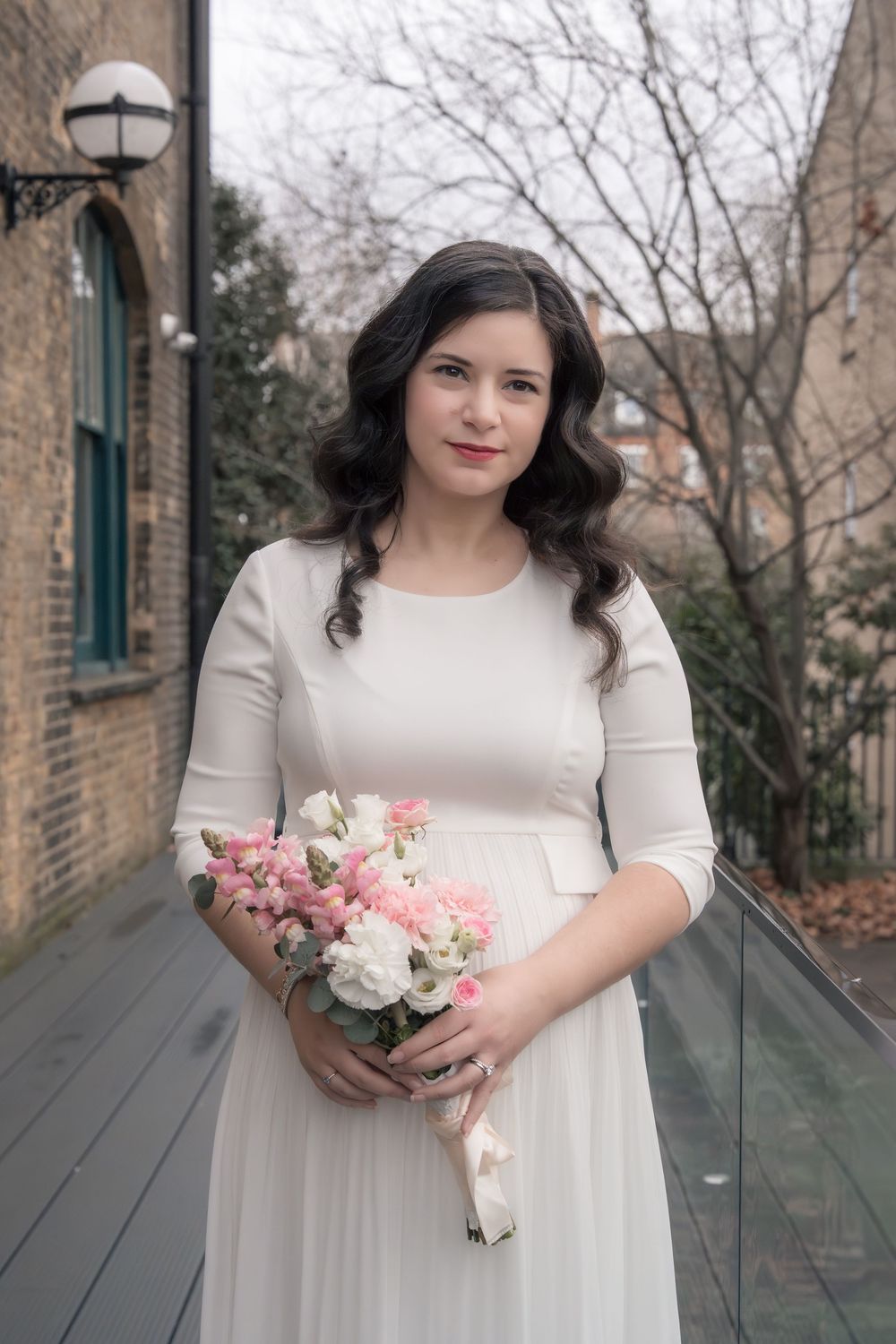 A bride in a white dress holds a pink and white bouquet while standing on a stone path outdoors.