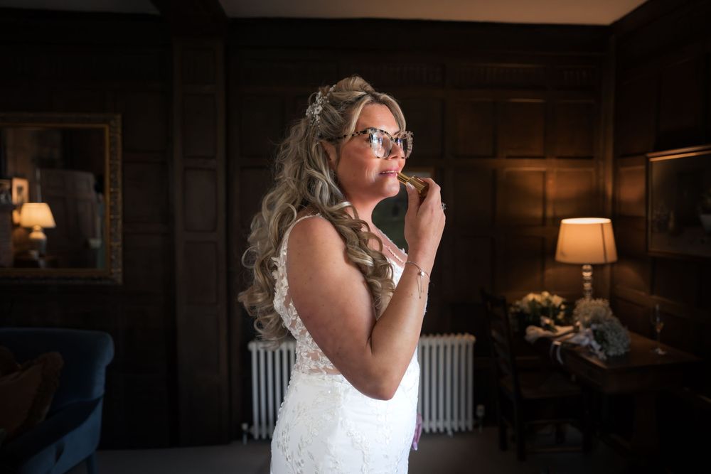 Bride in lace wedding dress and glasses stands in elegant wood-paneled room, looking up emotionally on her wedding day.