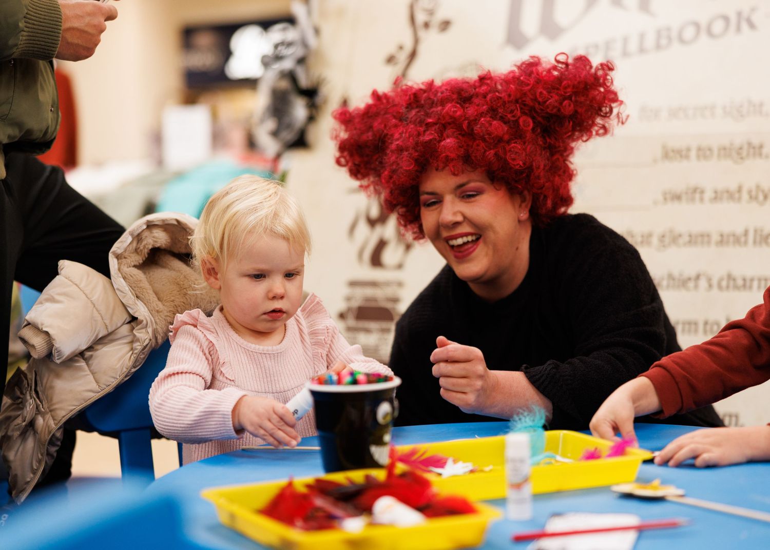 Children and adults gather around a colorful table engaged in an interactive learning or play activity.