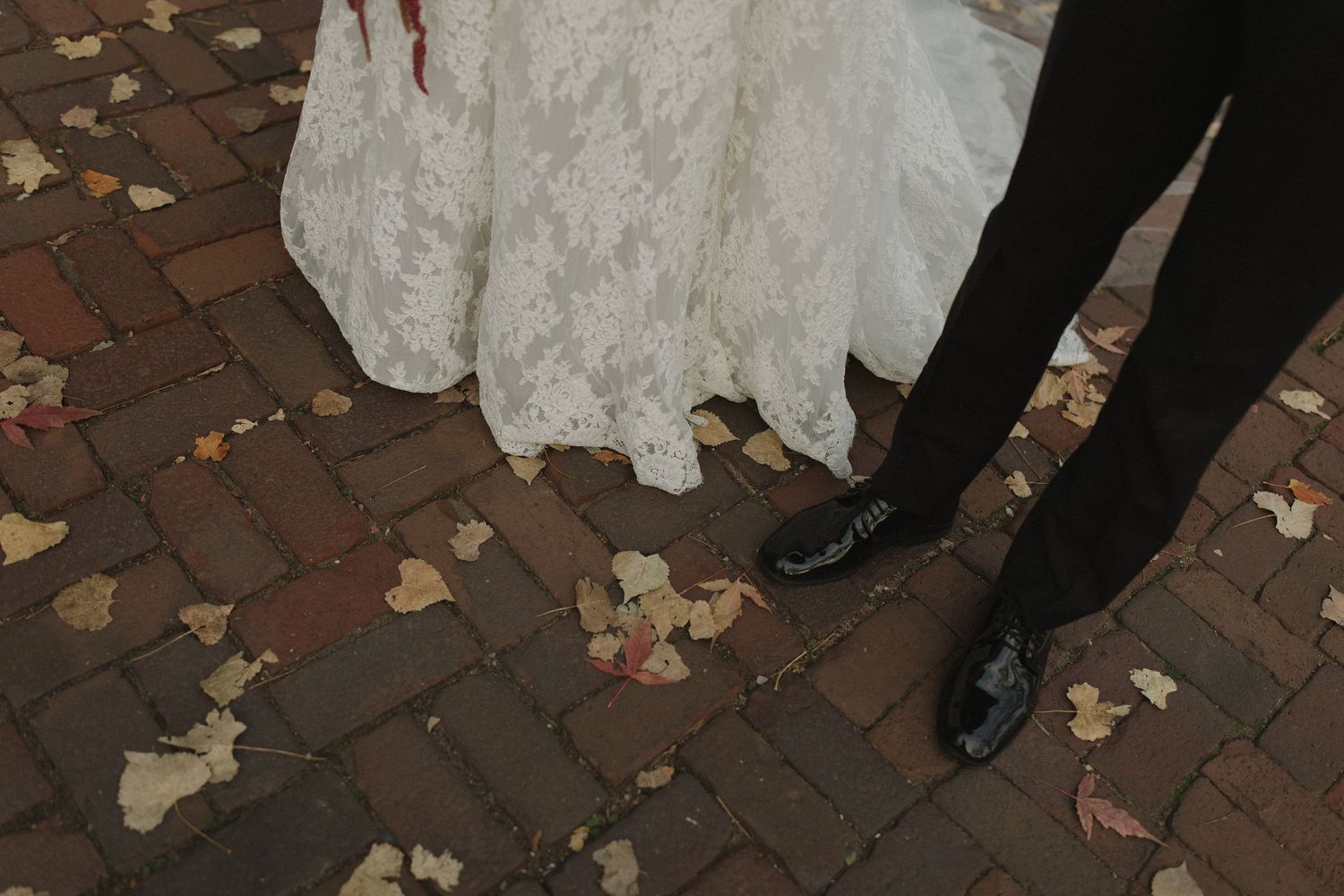 A couple in wedding attire poses together in a romantic outdoor setting with a mint green building in the background.